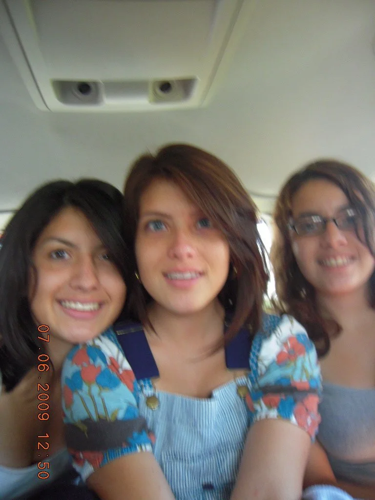 Three young women smiling for a photo inside a vehicle, with the ceiling and air vents visible above them.