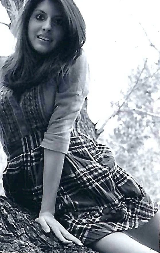 Woman with long hair in a plaid dress, sitting outdoors near a tree.