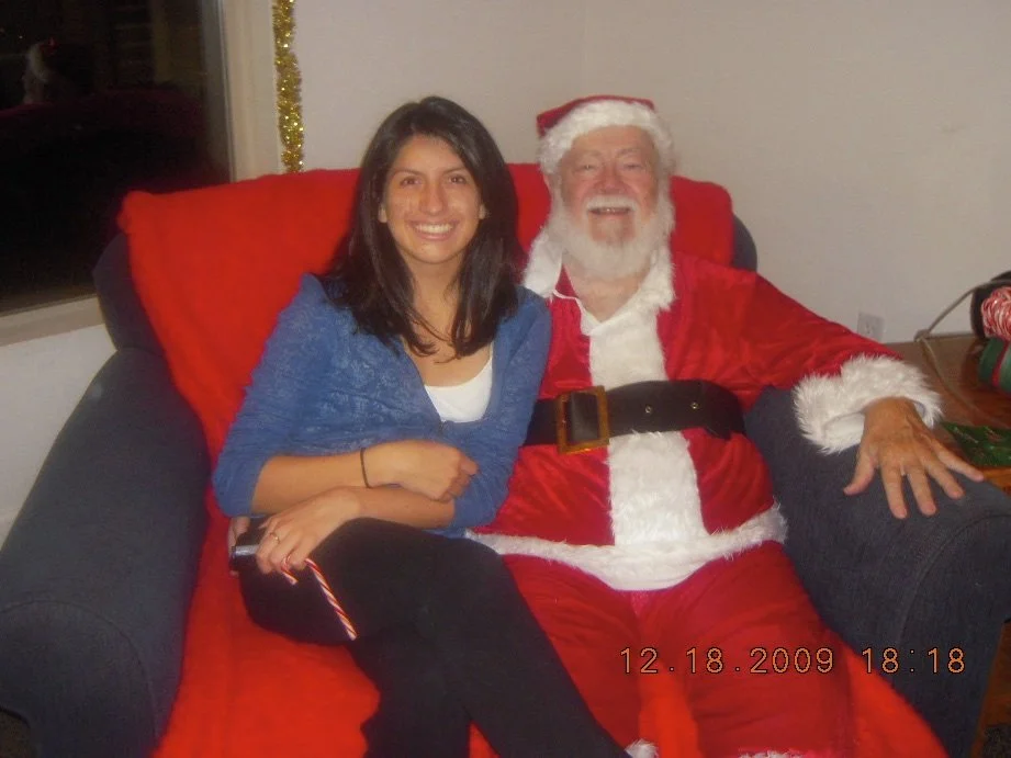 A woman sitting next to a man dressed as Santa Claus on a red and black sofa, smiling at the camera during a Christmas celebration in December 2009.