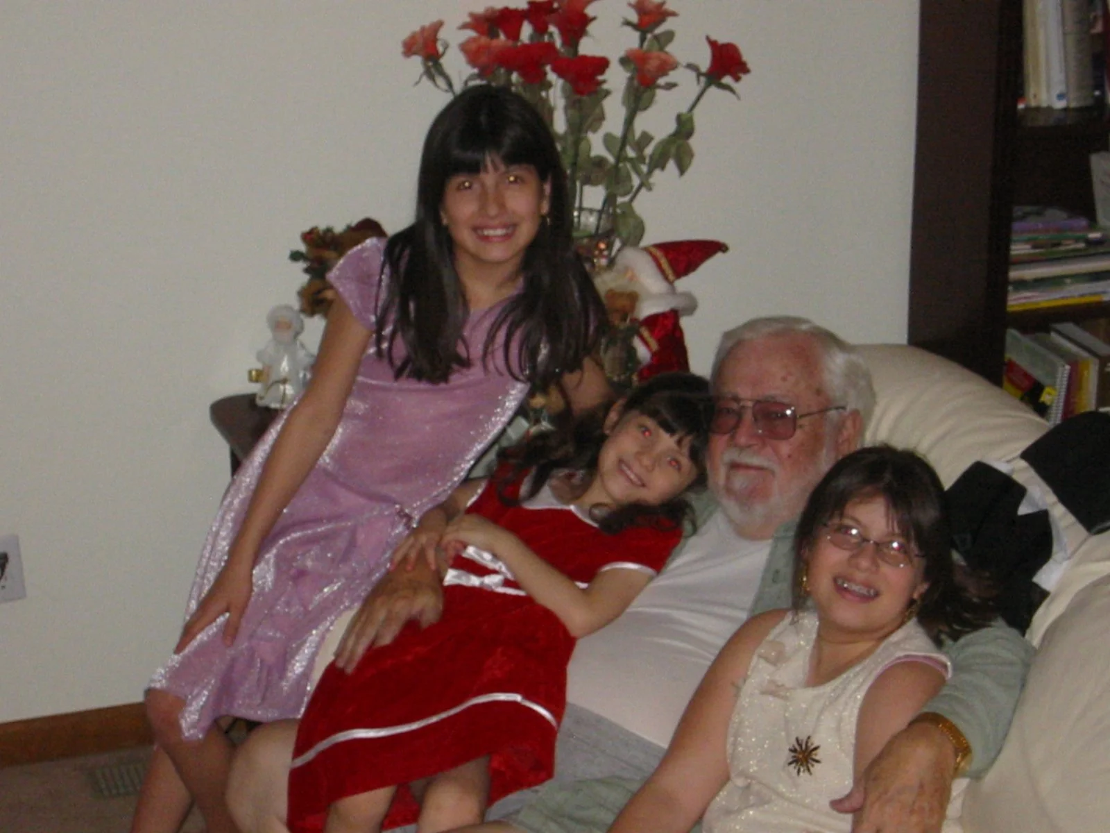 A family gathered in a living room for Christmas, with children and an elderly man, surrounded by Christmas decorations including a Christmas tree, Santa hat, and figurines.
