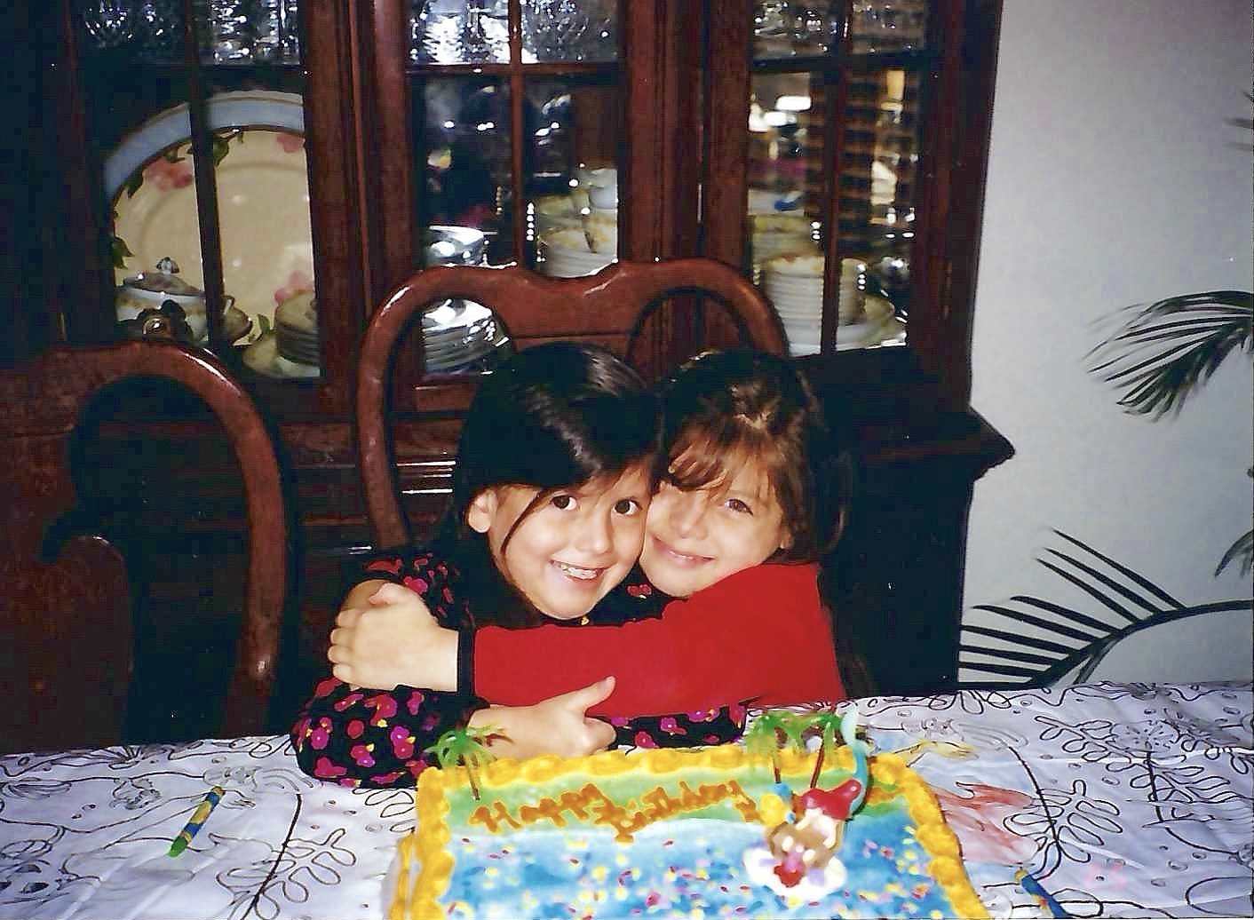 Two children hugging and smiling at a birthday party with a birthday cake in front of them.