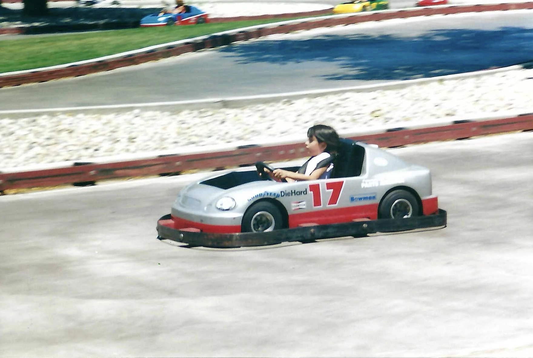 A person driving a small novelty car with racing numbers on a speedway track.