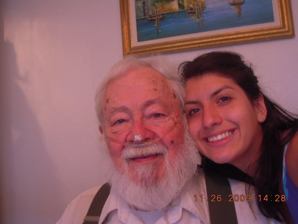 A young woman and an elderly man with a nasal oxygen tube are taking a close-up selfie together, smiling.