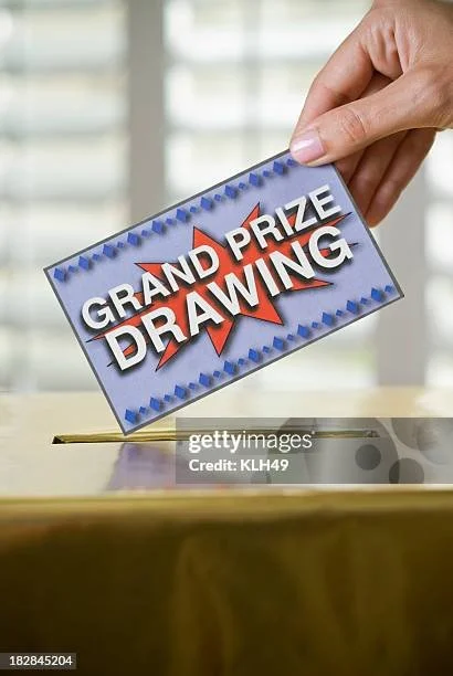 A hand placing a ticket into a raffle or prize box, with the ticket labeled 'Grand Prize Drawing' in bold letters.