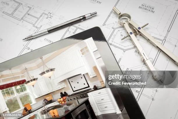 A tablet displaying a kitchen interior design on top of architectural blueprints, with a pen and a compass tool nearby.