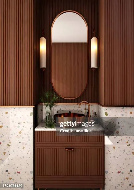 Bathroom vanity with a wooden cabinet, a round mirror, wall-mounted lights, a plant, and a faucet with a marble countertop.
