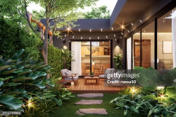 Outdoor patio of a modern house with string lights, surrounded by lush greenery, featuring seating and glass sliding doors.
