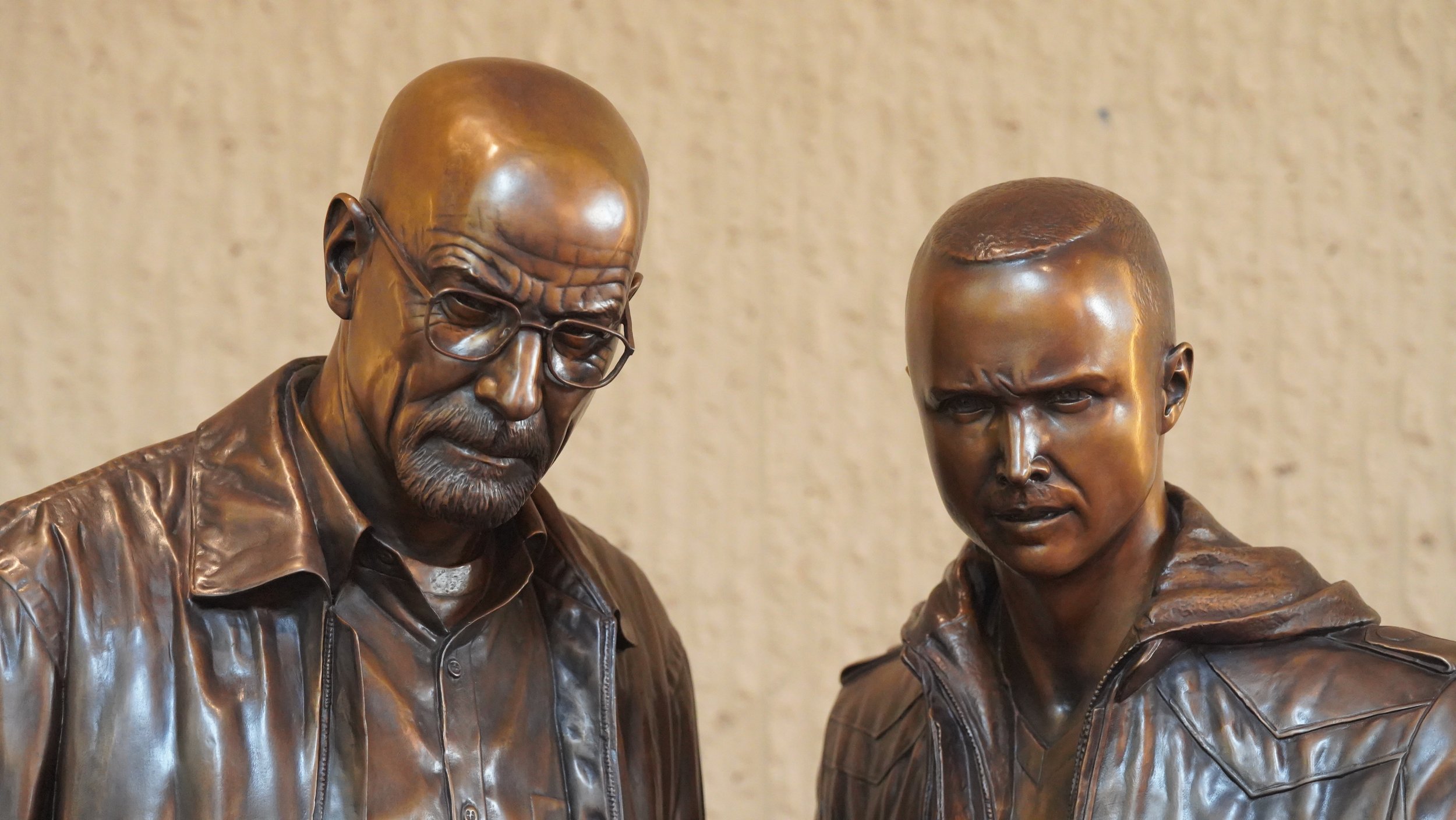 Bronze statues of two men, one with glasses and a beard, the other with short hair, both wearing jackets, appearing to look intently at something.