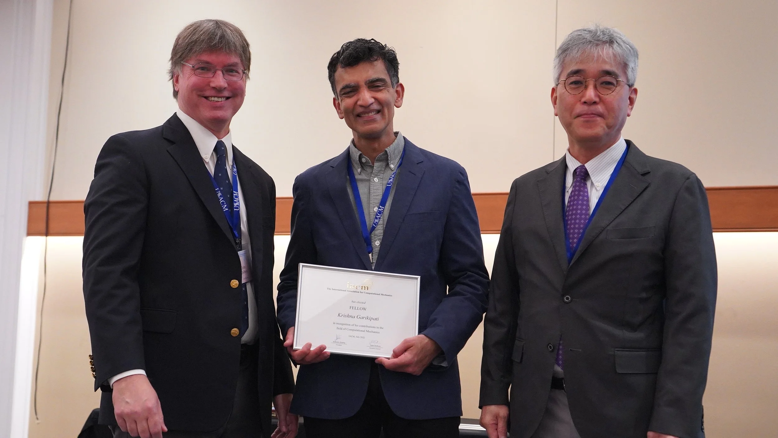 Three men in suits standing together, one holding a framed certificate, at an award ceremony or conference.