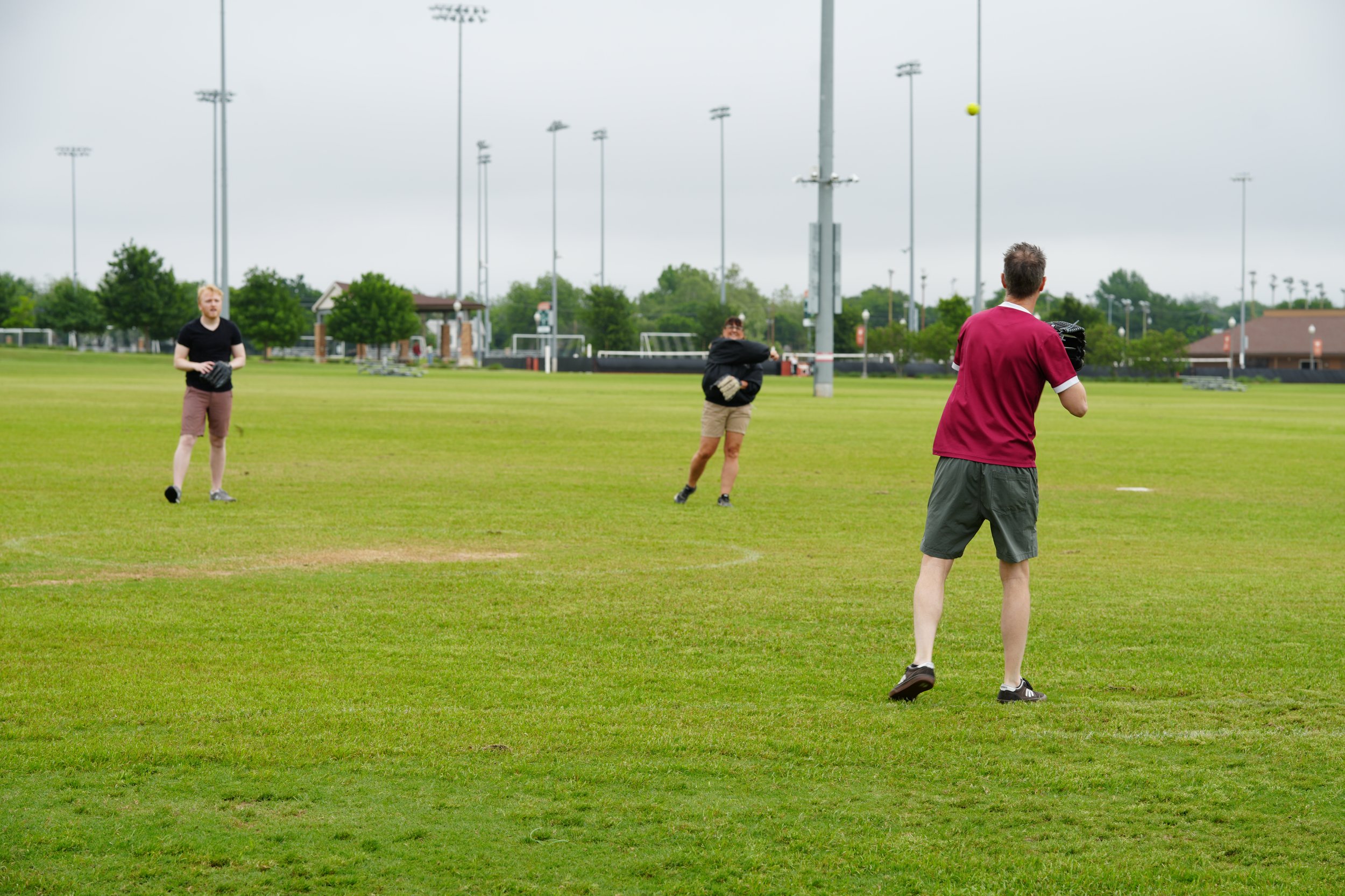 Three people at a baseball field practicing catching baseballs; two men and one woman, with baseball gloves.