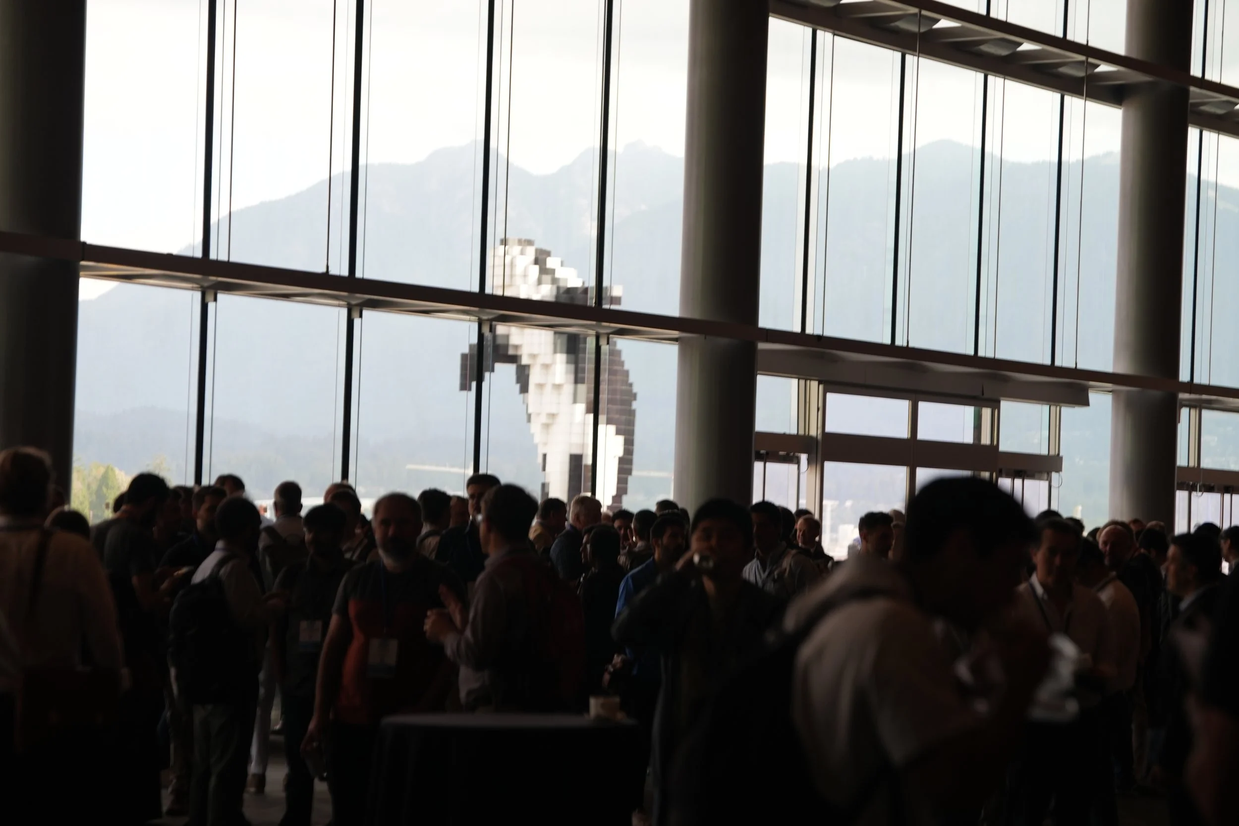 Crowd of people inside a modern building with large windows overlooking mountains.