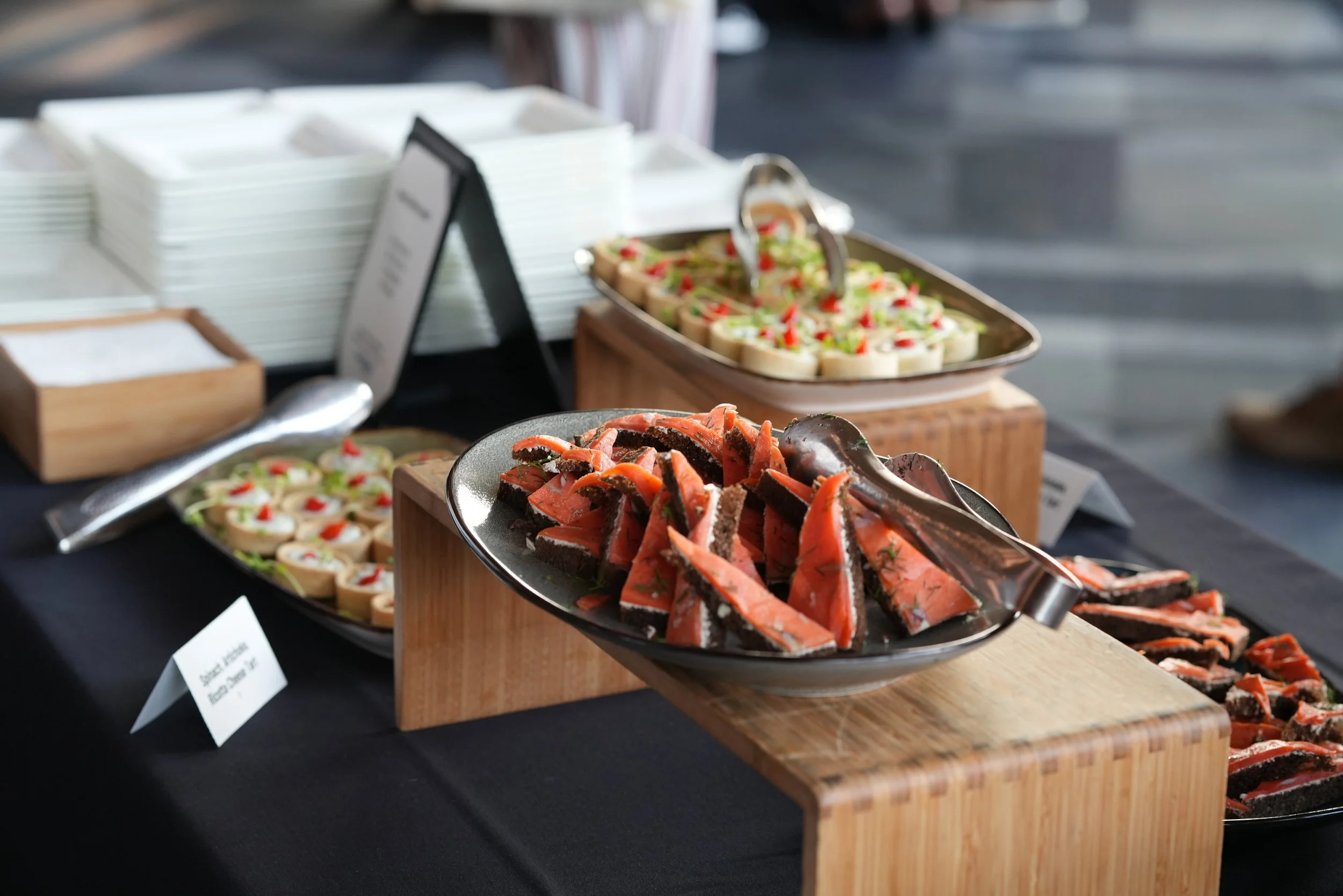 Assorted smoked salmon appetizers with garnish served on a silver platter at a buffet table.
