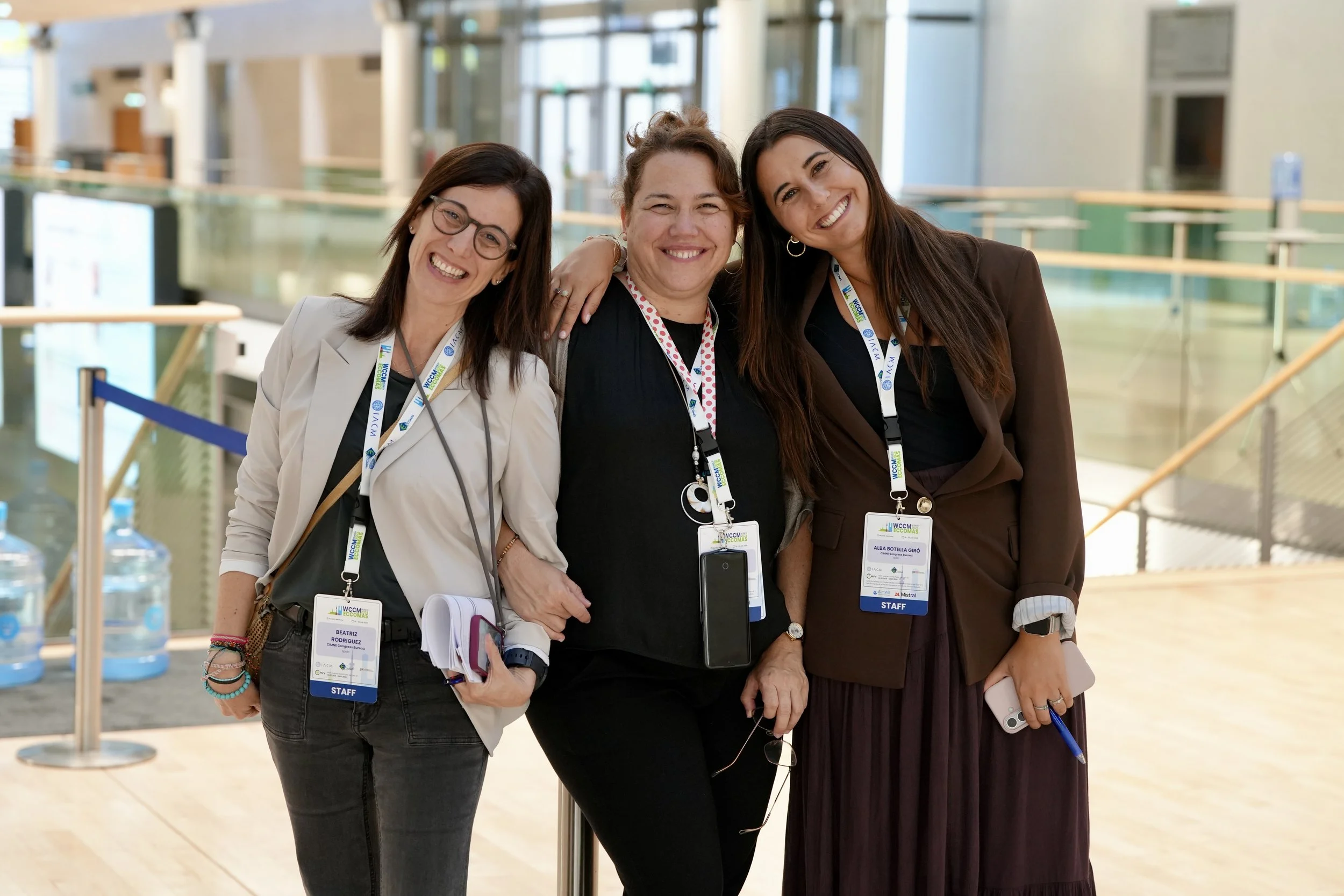 Three women smiling, standing close together at a conference, wearing security badges that say 'STAFF'.