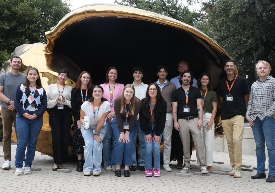 Team of research associates standing in front of a large, metallic oyster sculpture outdoors.