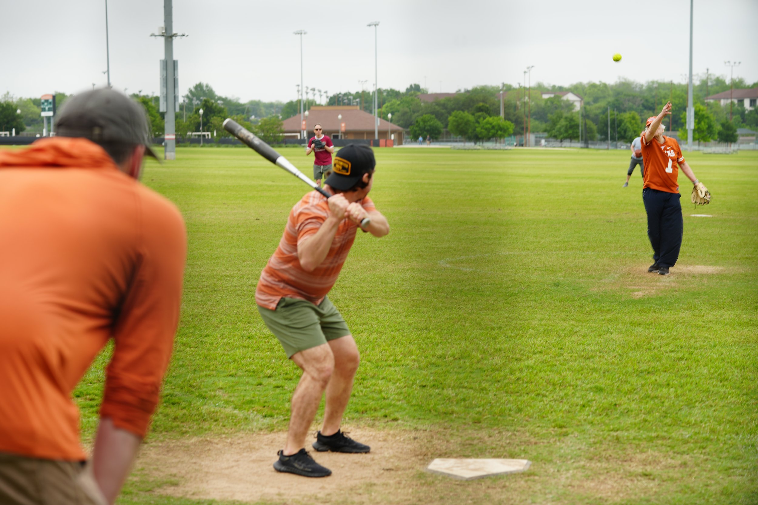 Young man pitching a baseball on a baseball field with teammates and a coach observing.