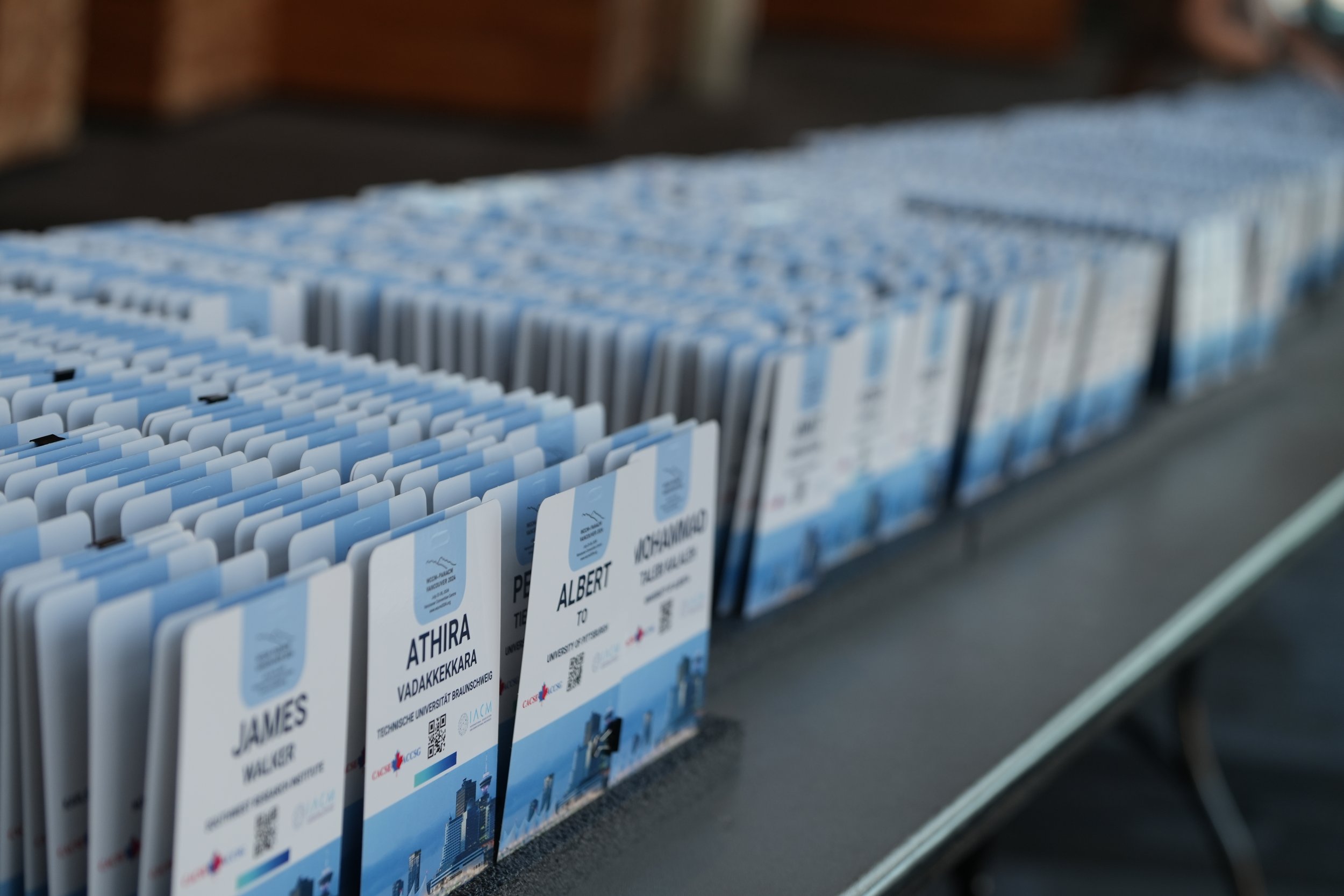 Close-up of conference name badges in a display, with names like Albert and Athira. The badges are mostly blue and white with cityscape graphics.