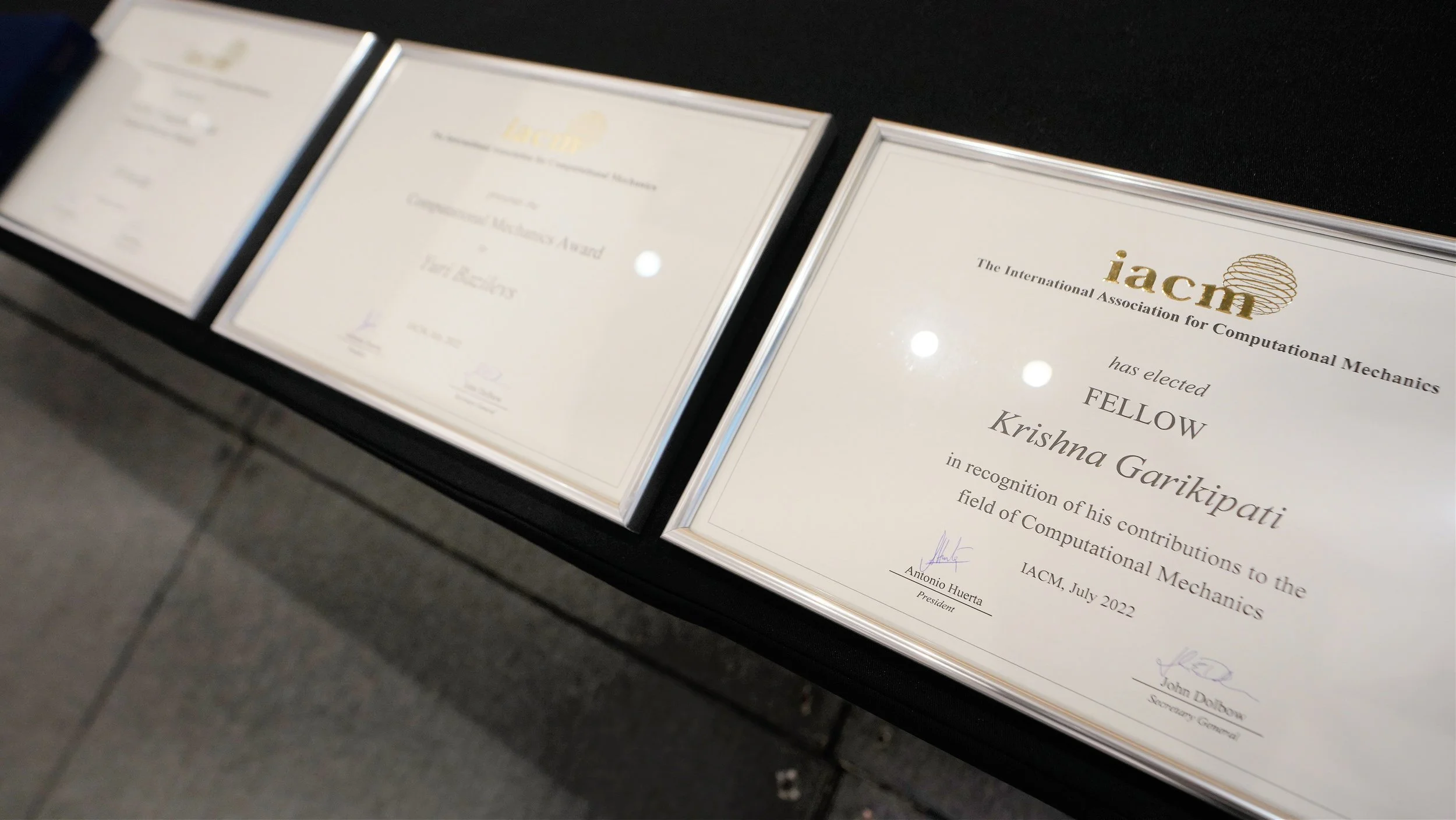 Framed certificates on a black table, including one from the International Association for Computational Mechanics awarded to Krishnna Garikipati.