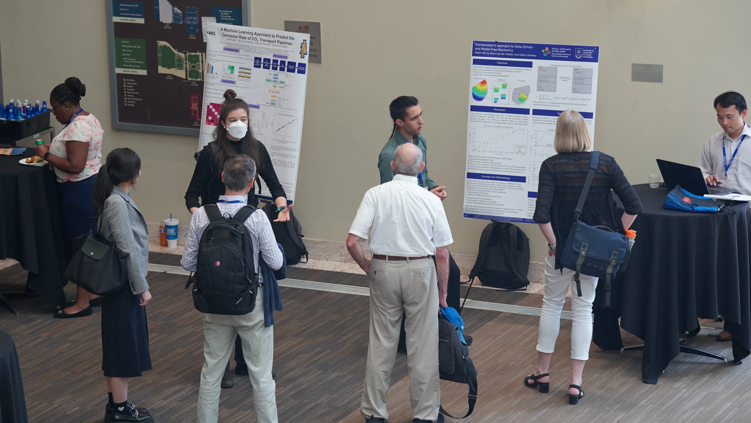 People attending a scientific poster presentation in a conference room, with multiple posters displayed on the wall and individuals engaged in discussions.