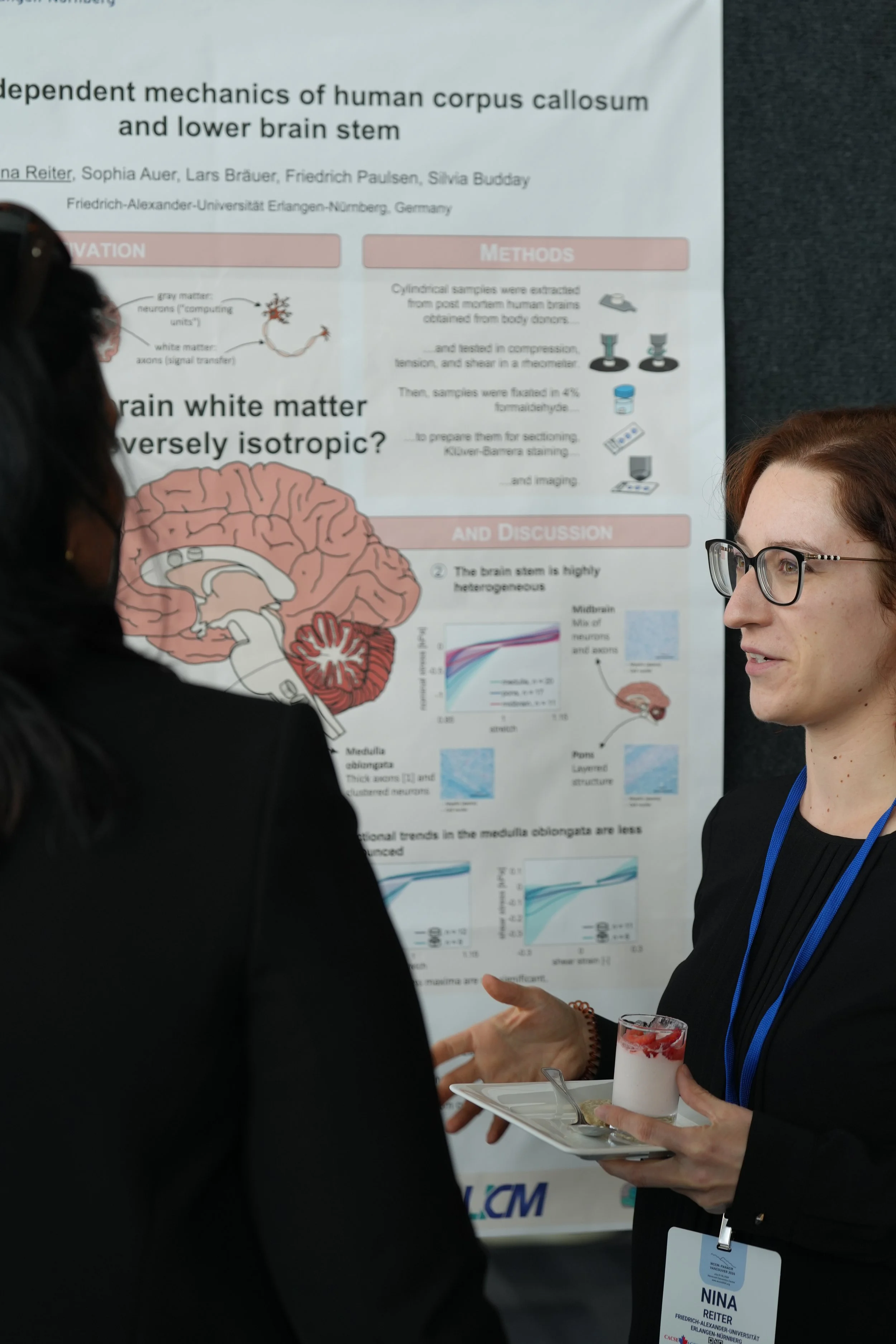 Two women are engaged in conversation at an academic conference, with a poster about neuroscience in the background during a poster session.