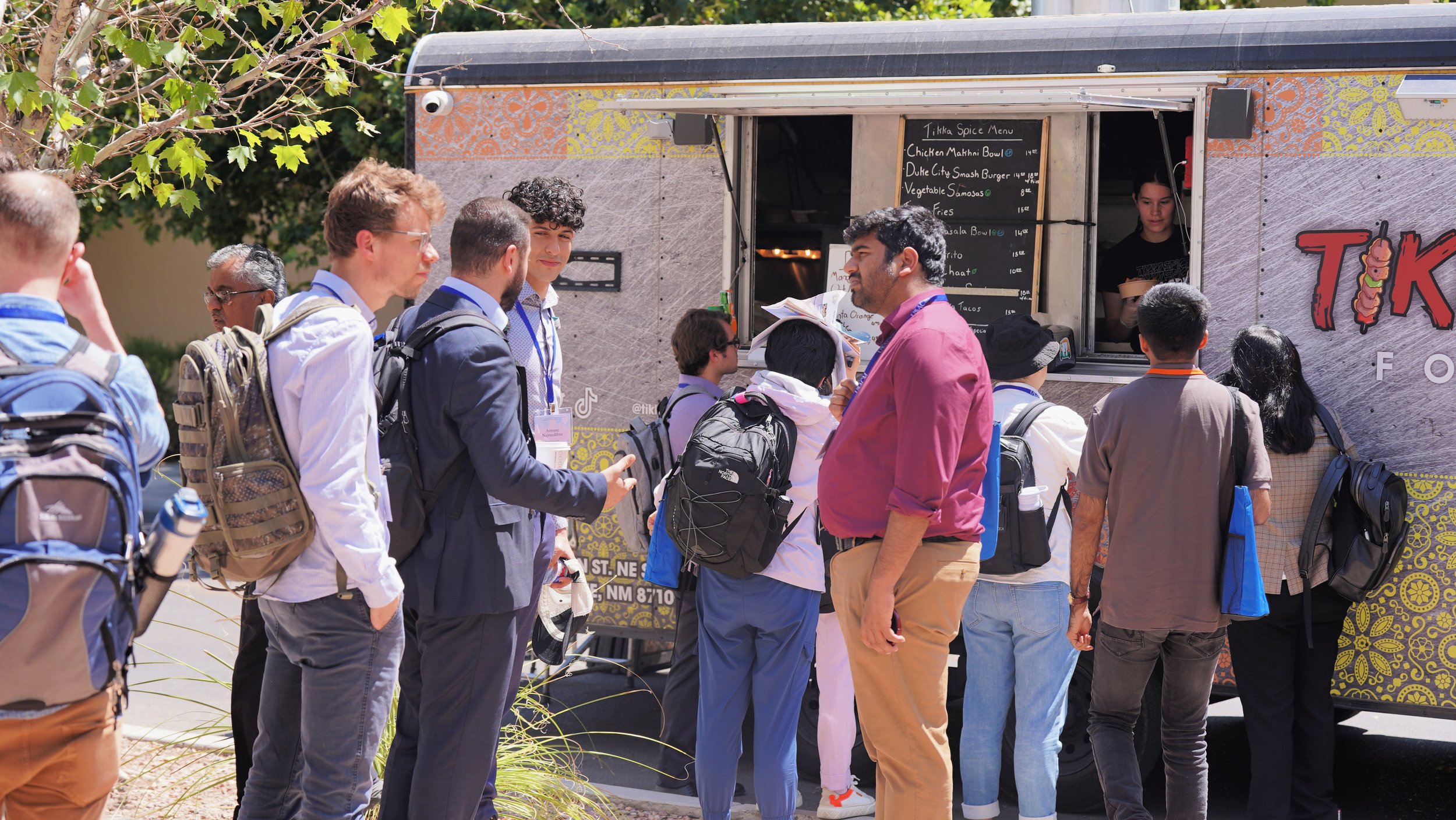 A group of people standing in line outside a food truck, ordering food and talking to the staff inside.
