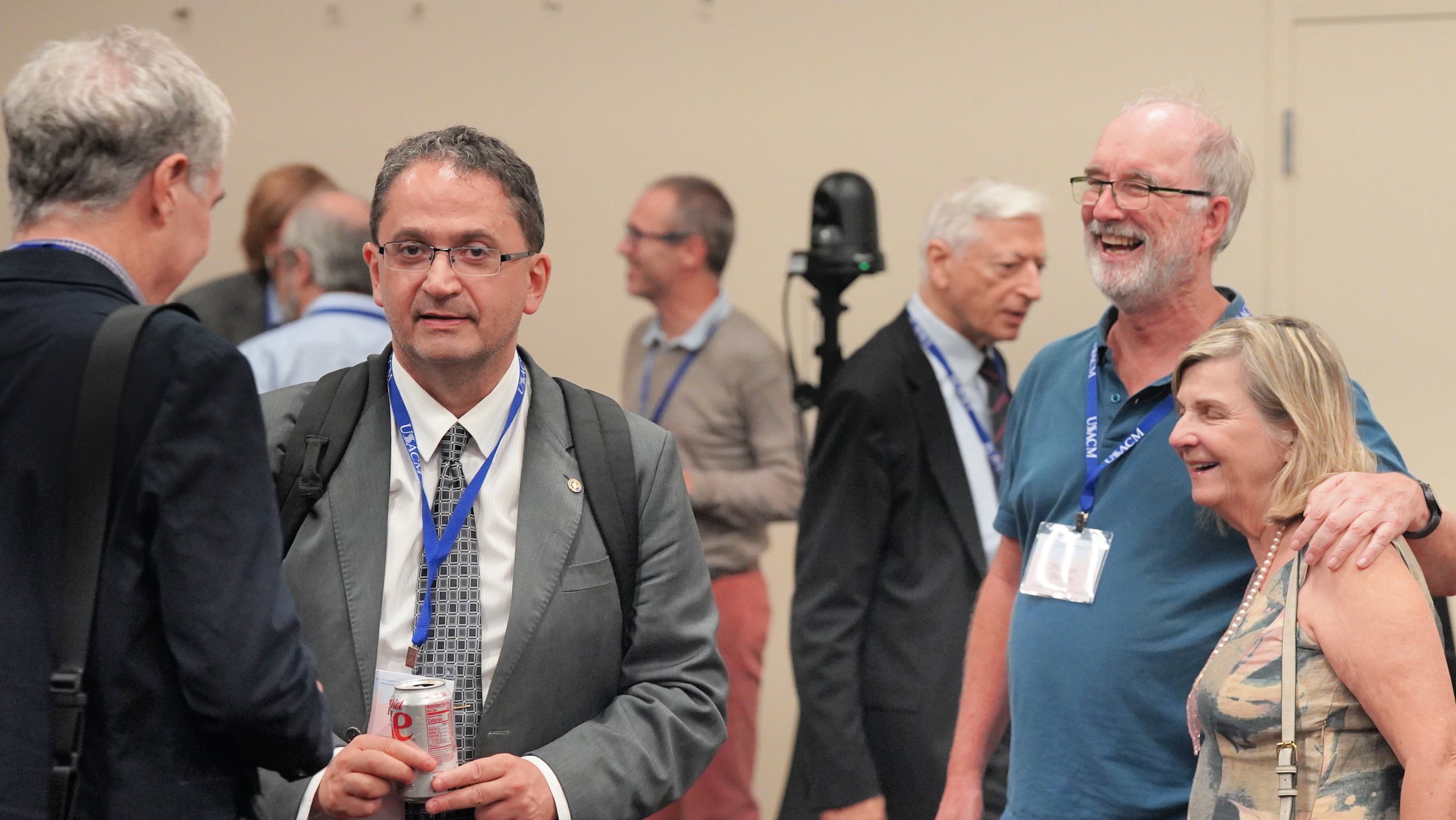 Group of people at a conference socializing and smiling, wearing name badges and lanyards.