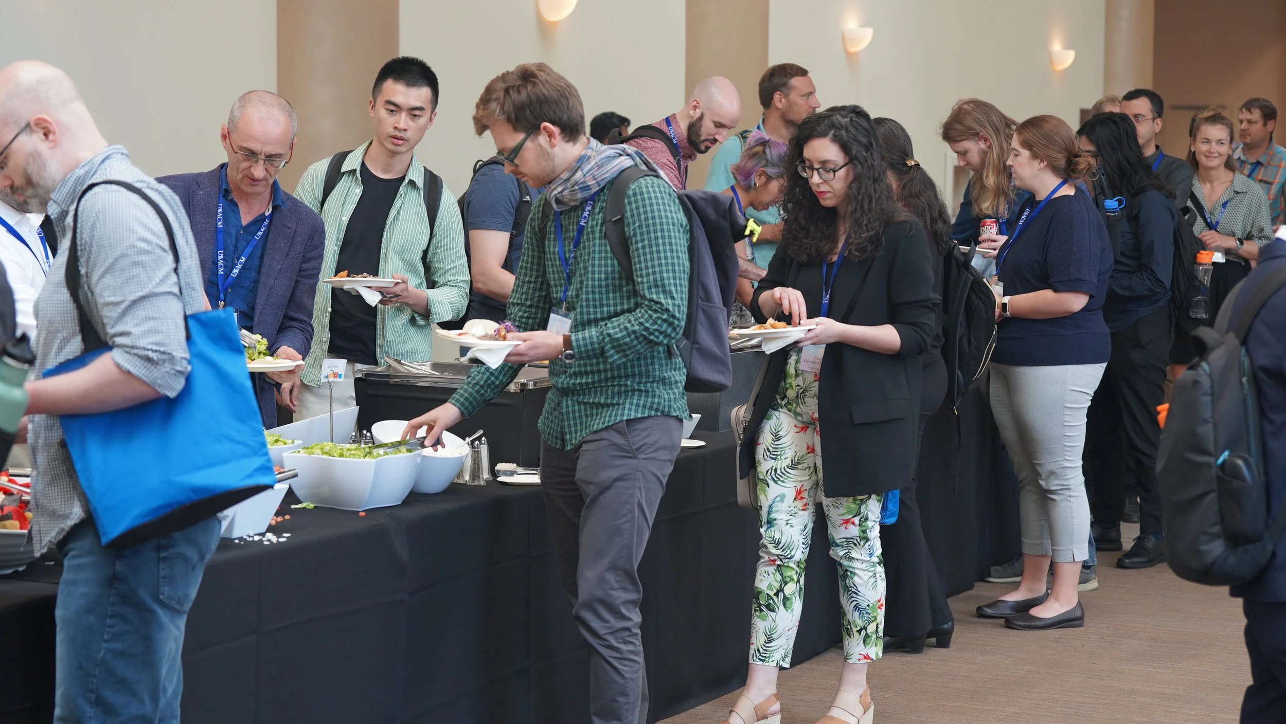 People in line at a buffet table with salad and food items, in a conference or event setting.