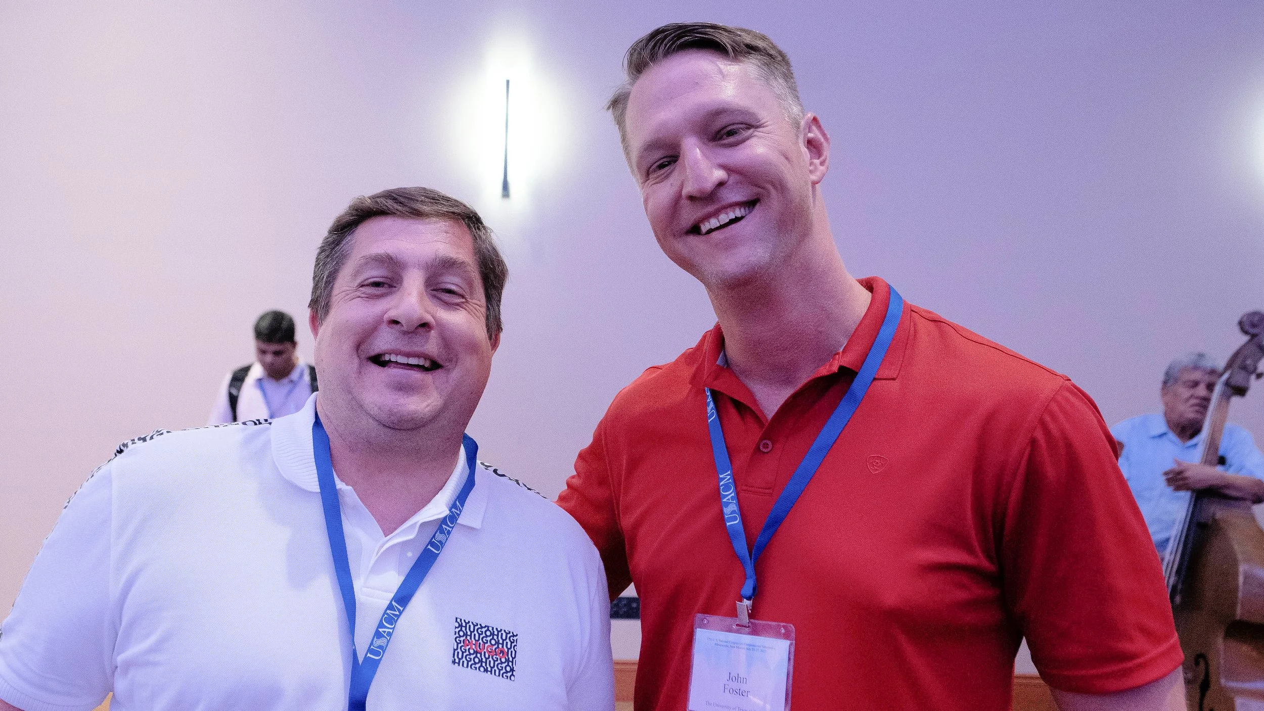 Two smiling men posing at an event, wearing conference badges around their necks.