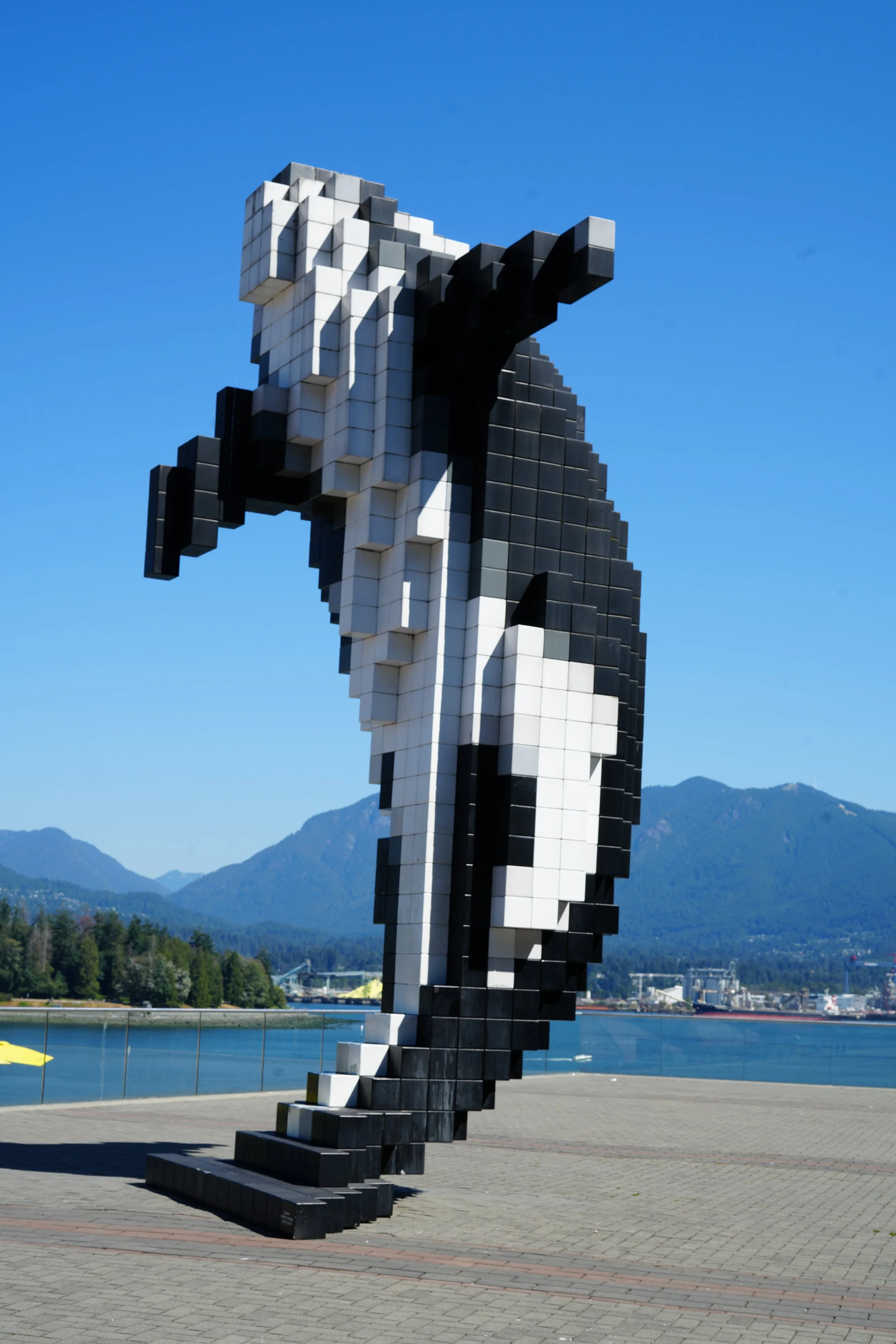 A large pixelated sculpture of a woman with a raised fist, made of black, white, and gray cubes, standing outdoors against a mountain and blue sky background.