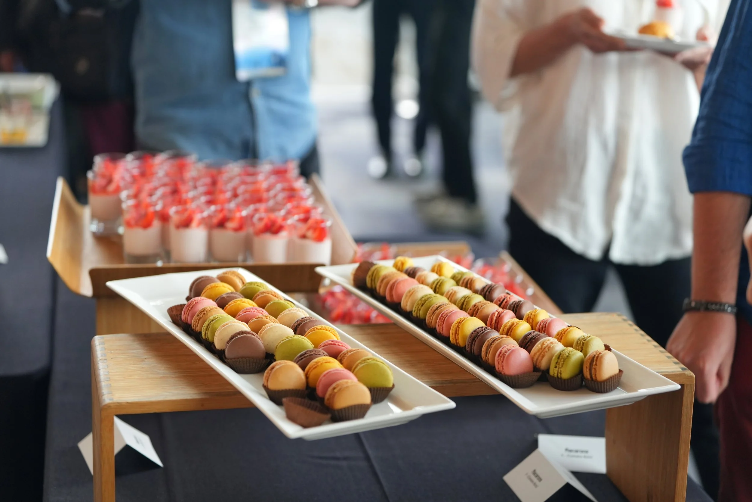 Display of colorful macarons on white trays at a booth.