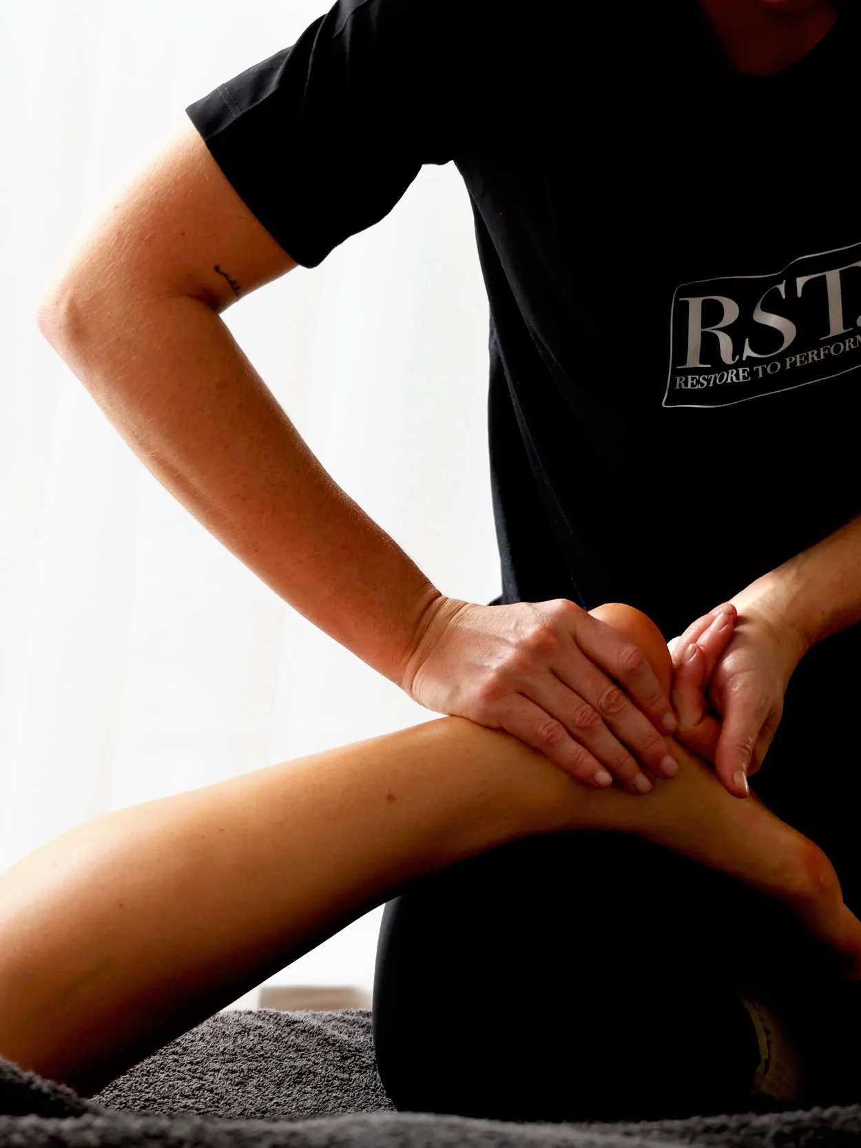A massage therapist providing a massage therapy session to a person lying face down.