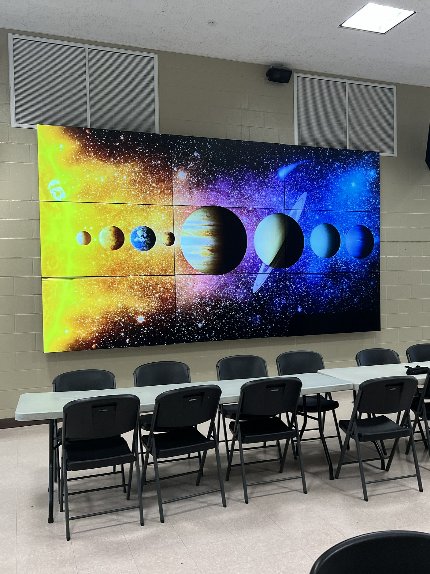 A large digital display shows an artistic depiction of the planets in the solar system with a colorful cosmic background. The space scene includes the sun on the left and the planets lined up from left to right, with the background blending yellow, purple, and blue hues.