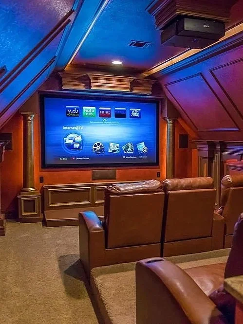 Home theater room with a large flat-screen TV, leather recliner chairs, and wood-paneled walls.