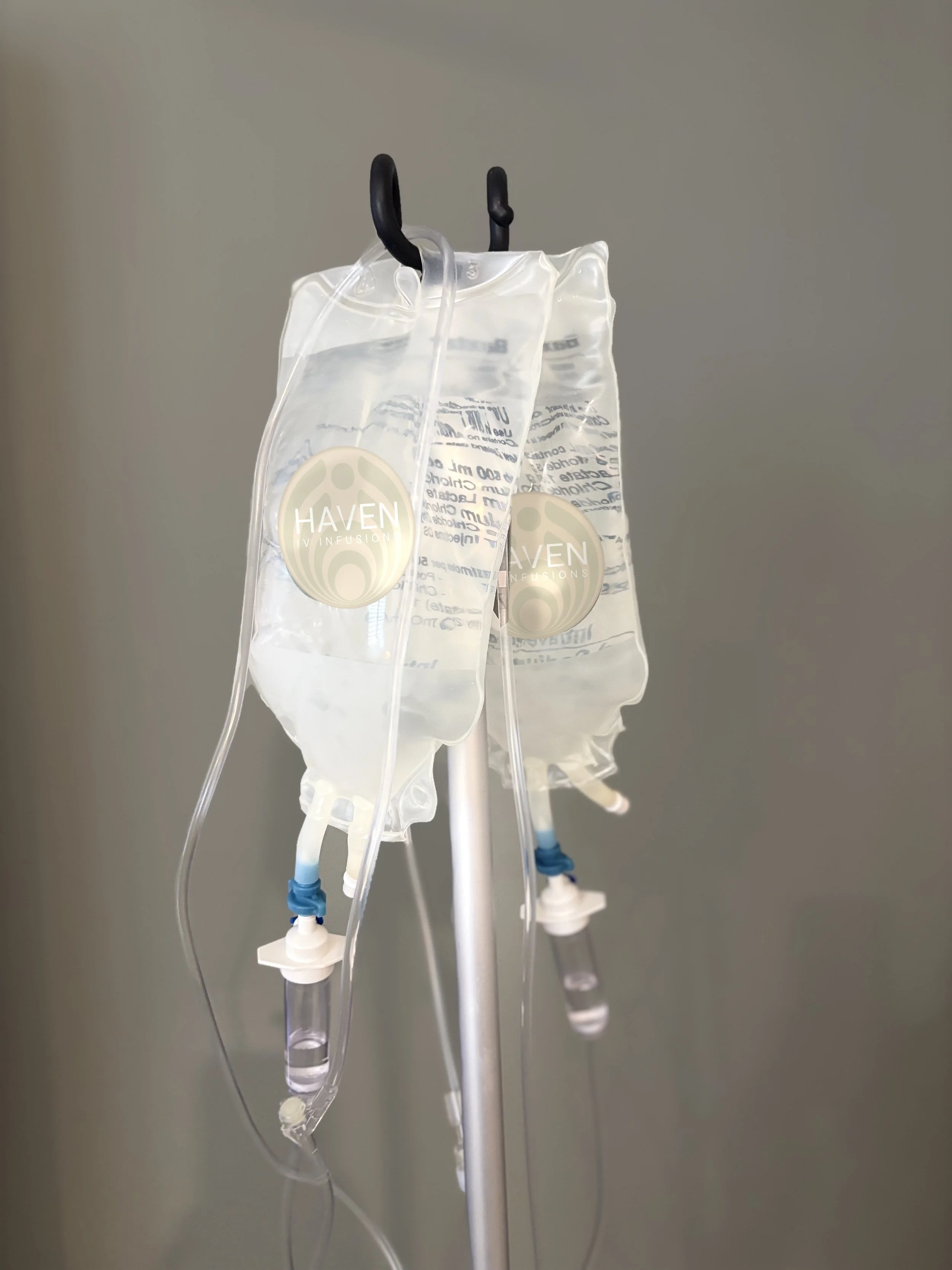 Medical IV drip bags hanging on a stand with tubing and connectors, labeled 'HAVEN INFUSIONS'.