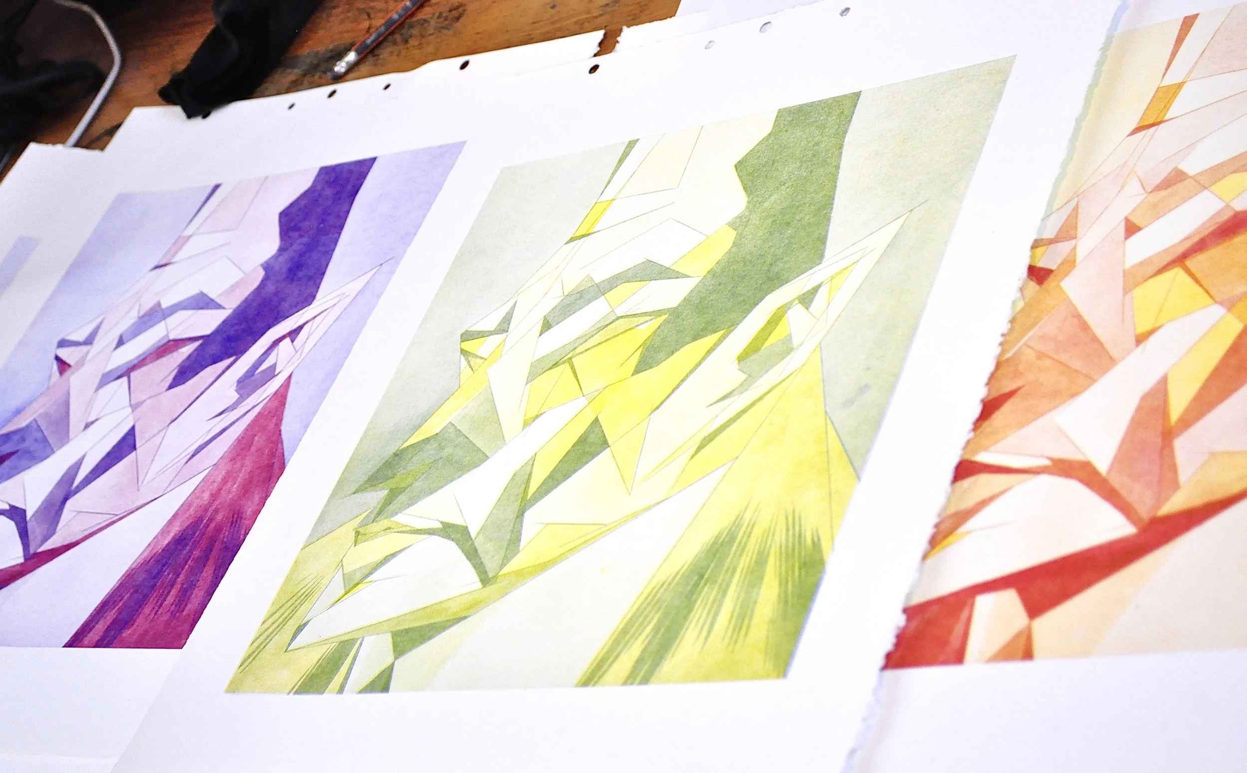 Hojas con dibujos de formas geométricas y colores vibrantes, sobre una mesa de madera.