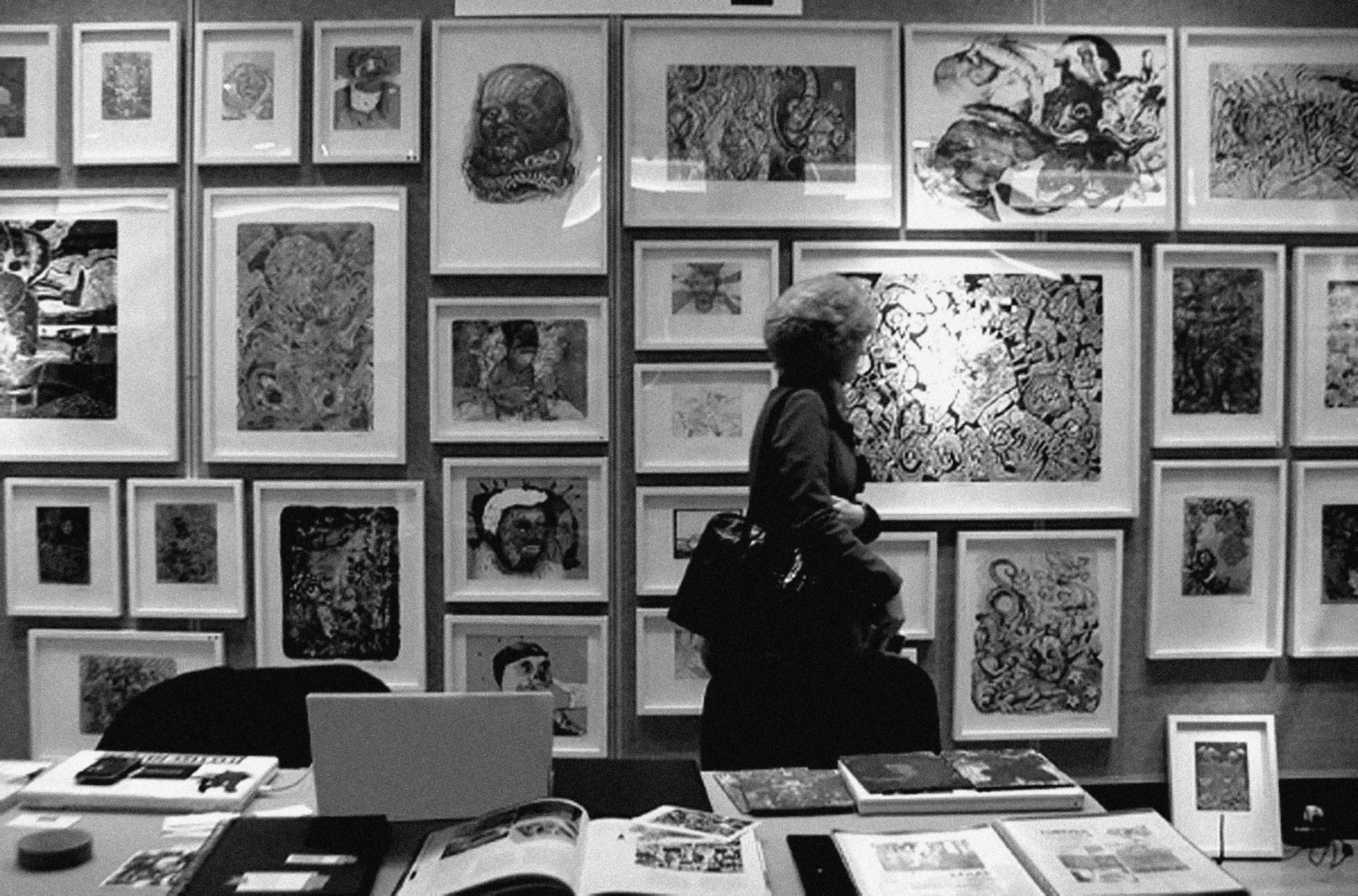 Una exposición de arte con varias obras enmarcadas en la pared y un visitante observando la muestra, en un entorno de galería o museo.