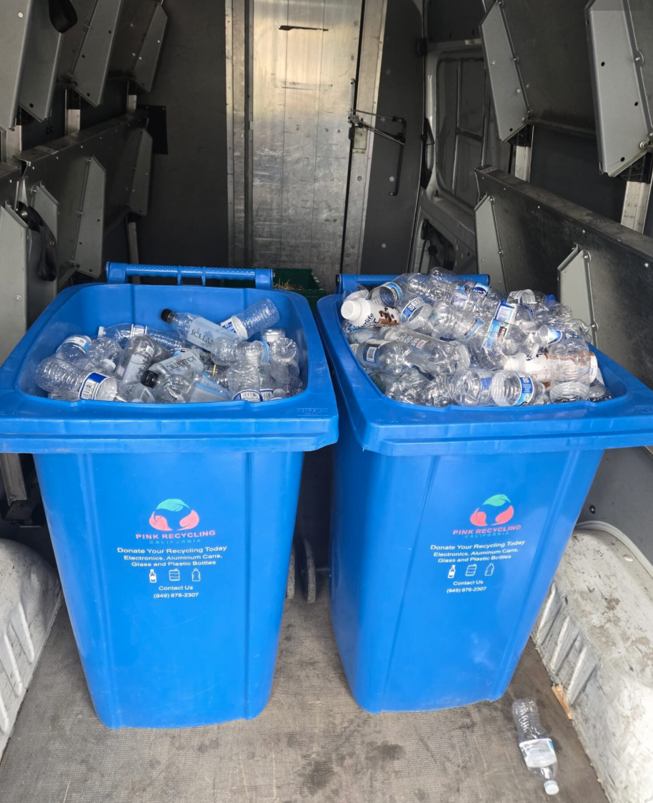 Two blue recycling bins filled with empty plastic water bottles inside a recycling truck.