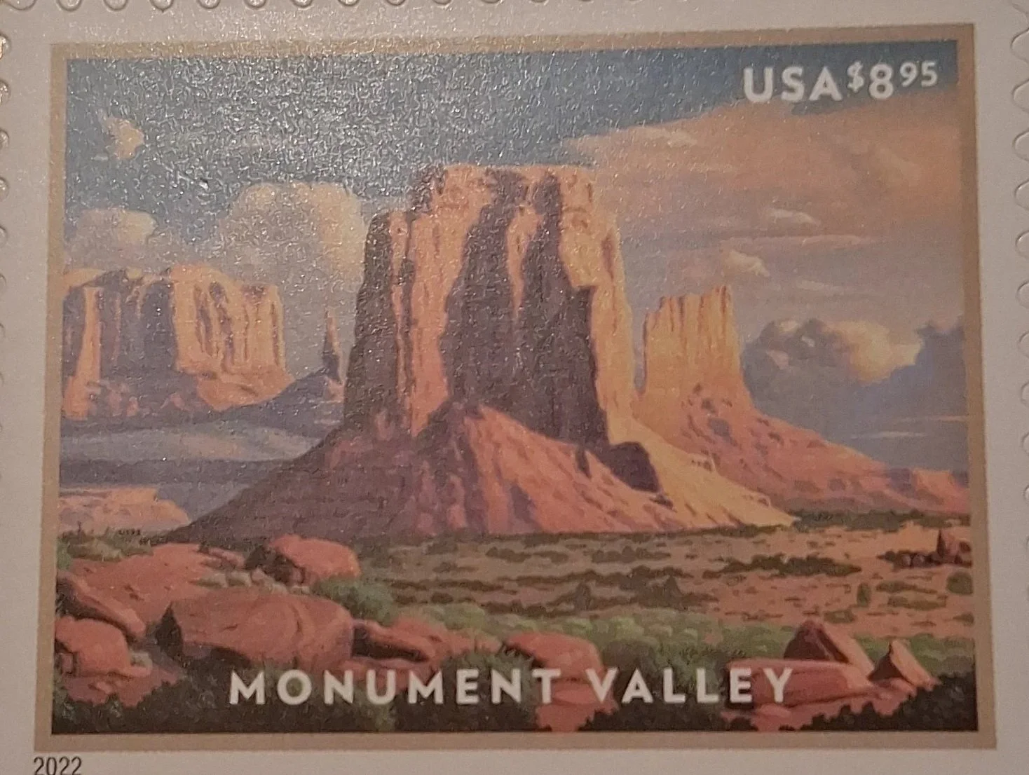 A postage stamp featuring a landscape scene of Monument Valley with towering red sandstone formations, desert terrain, and a partly cloudy sky. The stamp has a denomination of $8.95 and is marked "USA".
