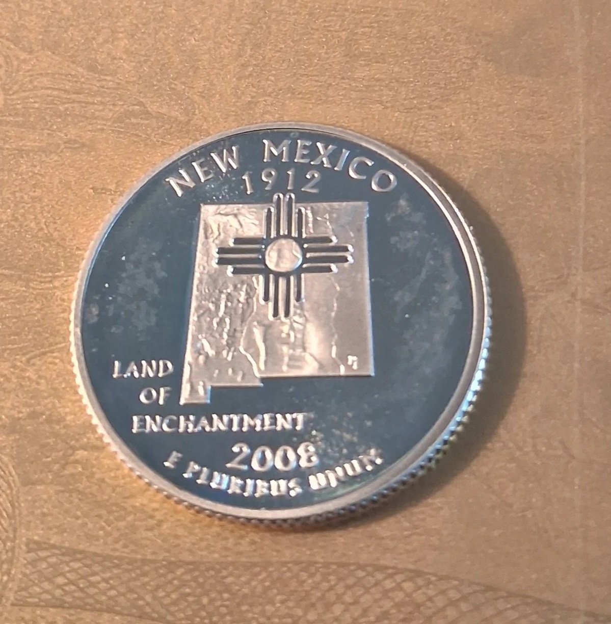 a silver commemorative coin with the text "New Mexico 1912 Land of Enchantment 2006" and an image of the Zia sun symbol over a map of New Mexico