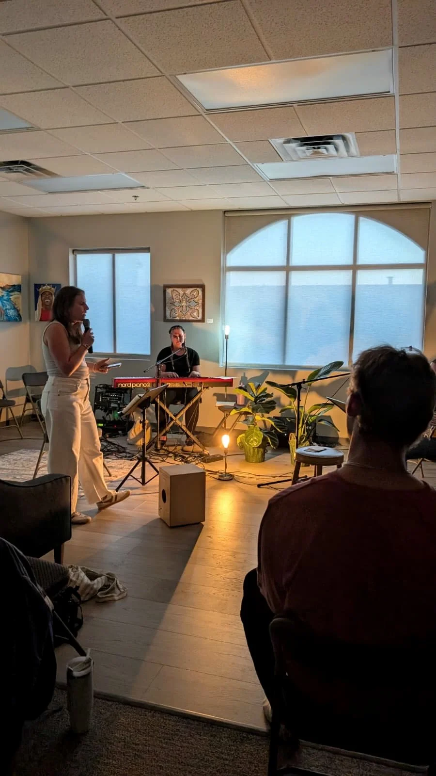 Musician and vocalist performing in a cozy indoor setting with warm lighting, plants, and artwork on the wall.
