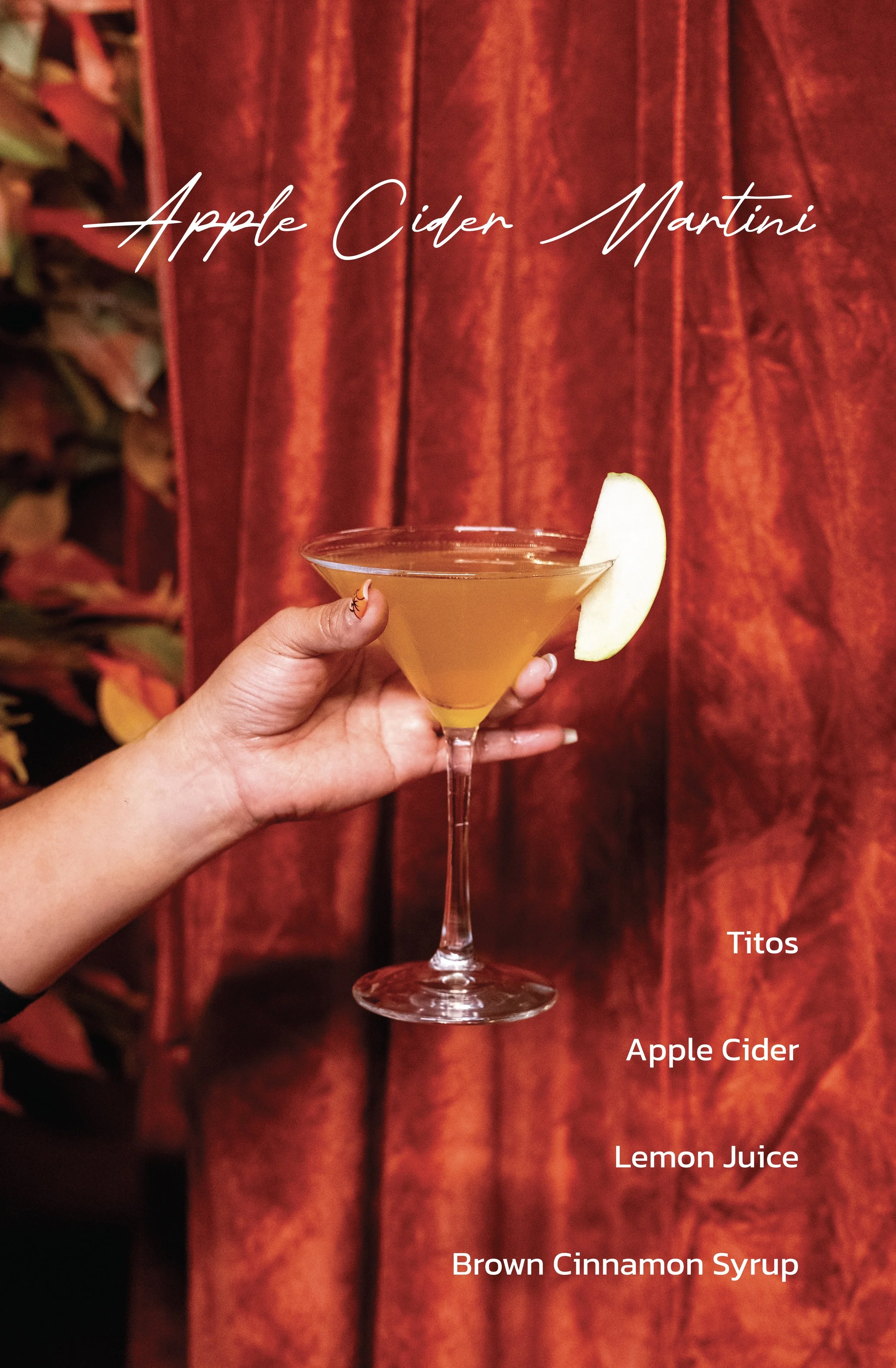 A hand holding a cocktail glass filled with a yellowish drink, garnished with a slice of apple on the rim, against a red curtain background. Text on the image reads 'Apple Cider Martini' and ingredients are listed as 'Titos', 'Apple Cider', 'Lemon', and 'Brown Cinnamon Syrup'.