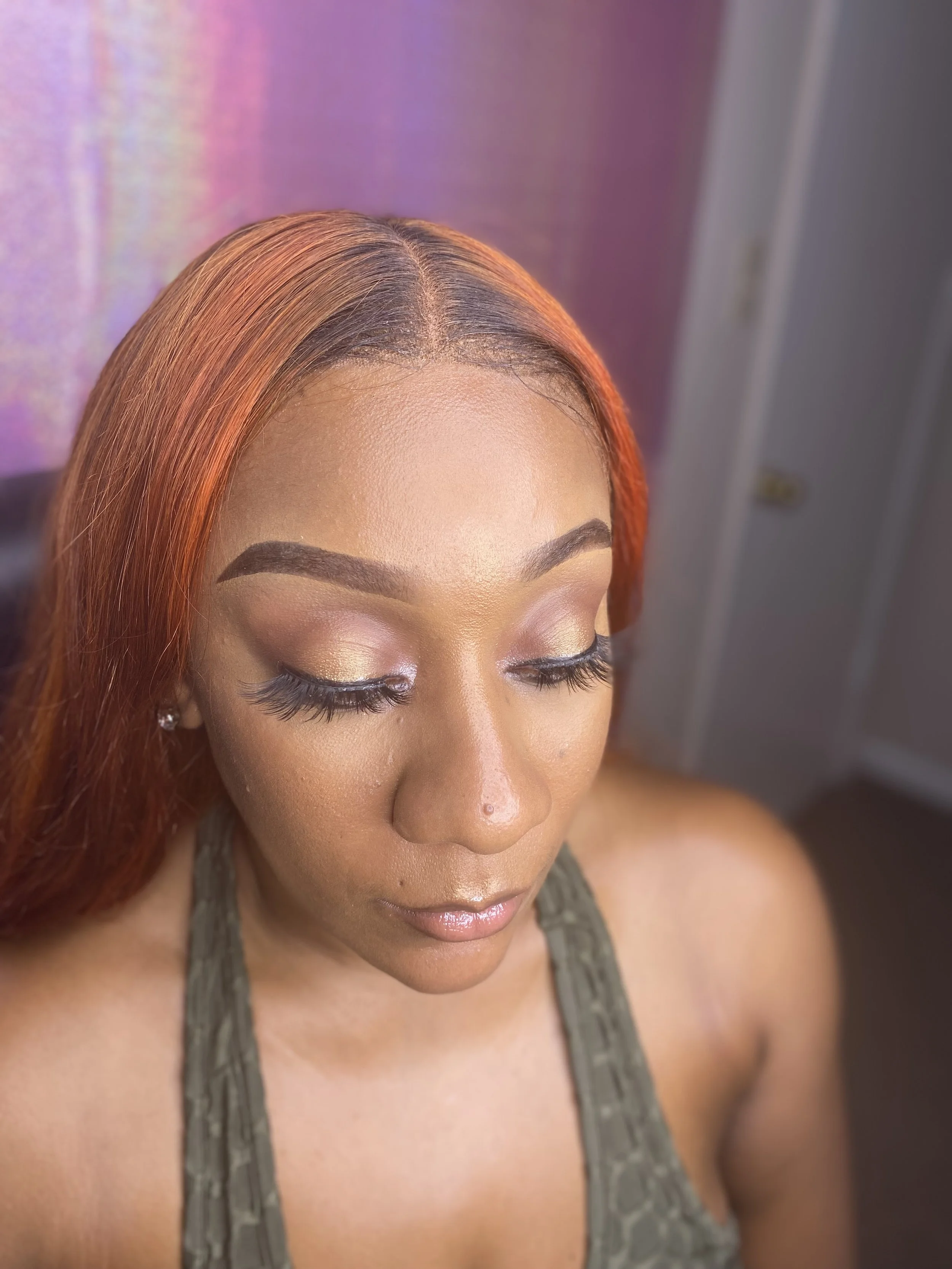 Close-up of a woman's face with orange hair, makeup, and closed eyes, wearing a gray tank top.