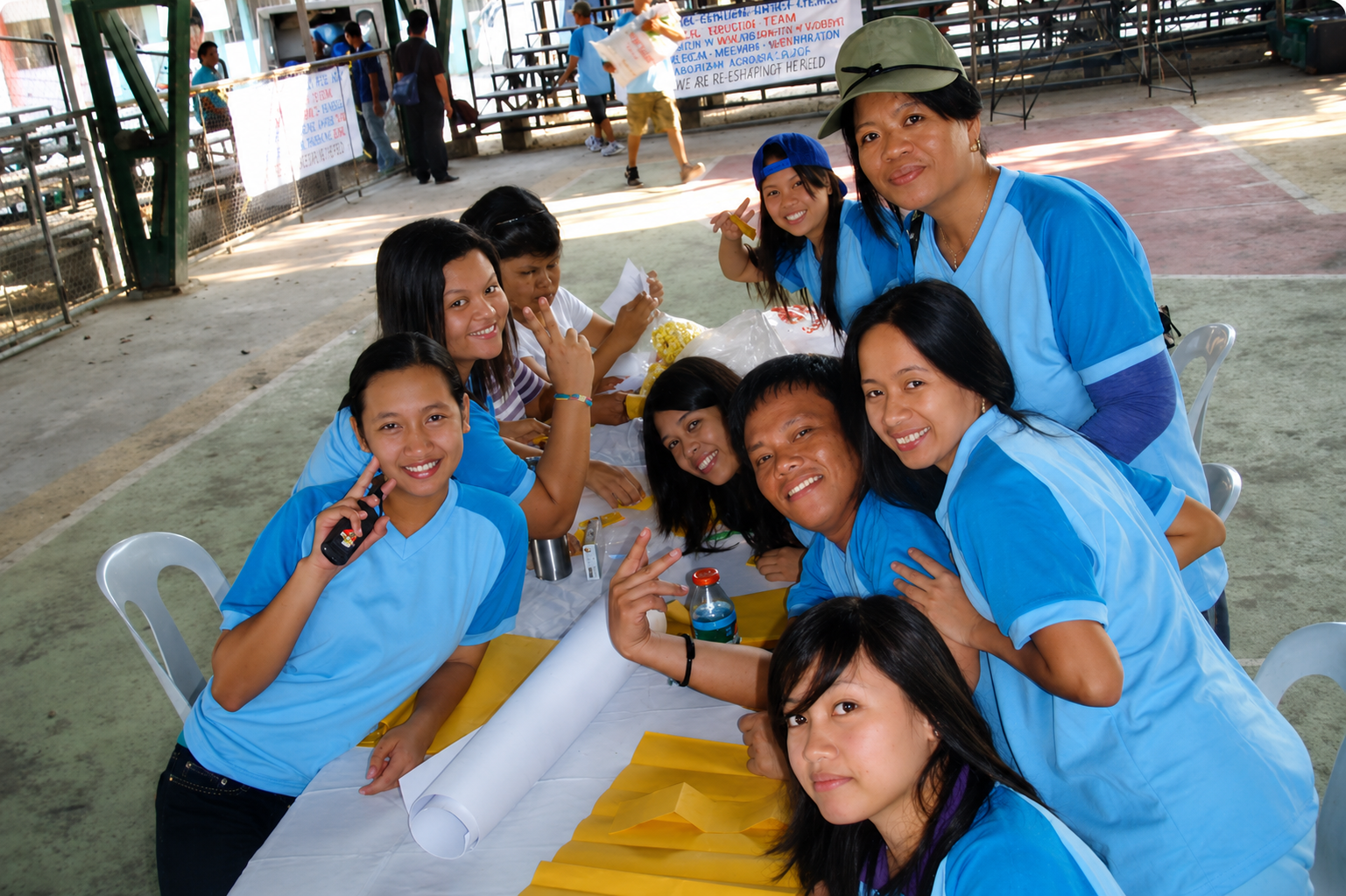 Group of smiling people in blue shirts gathered around a table at an indoor event, celebrating or having a meal.