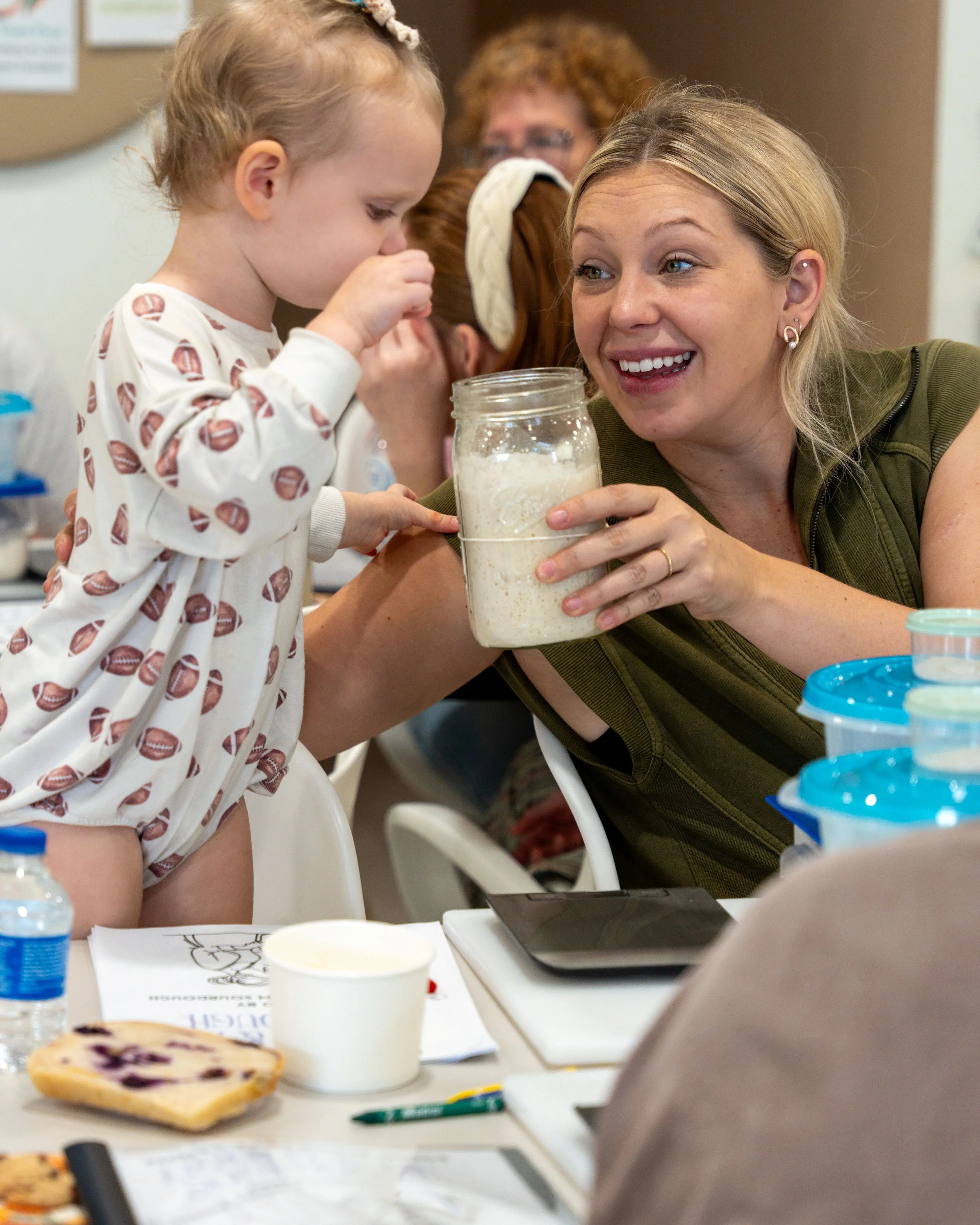 A young girl and woman explore sourdough starter together at a table.