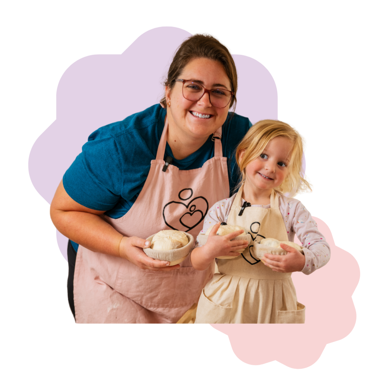 A woman and young girl bake together in aprons, holding bowls of dough.