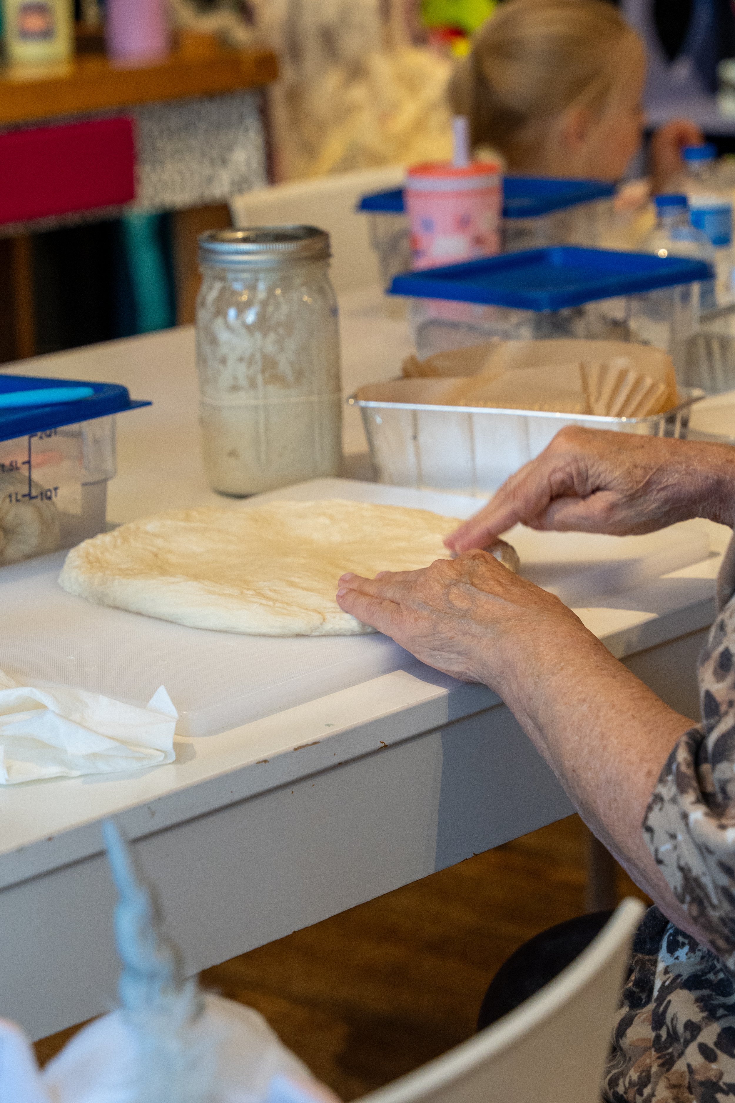 Hands stretch sourdough on a work surface beside flour and baking ingredients.