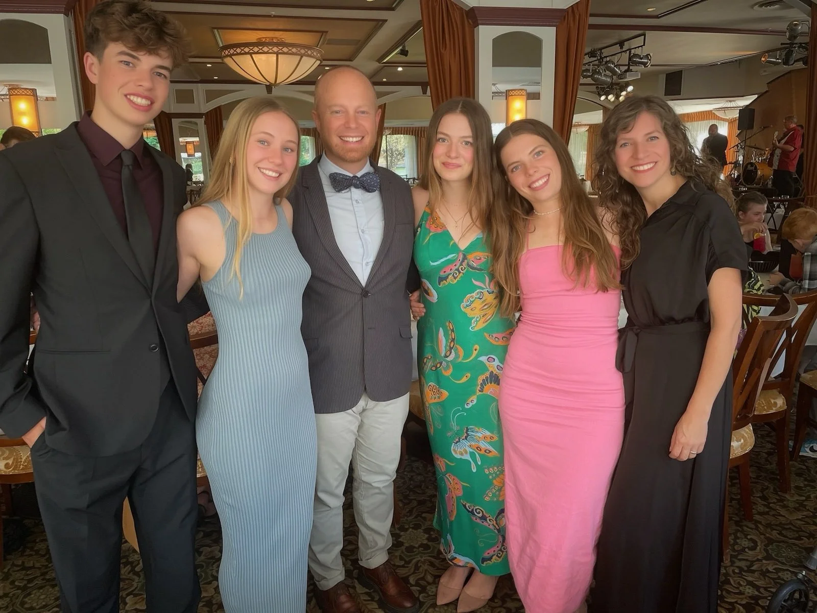 Group of six people smiling and posing together indoors, dressed in formal and colorful attire, at a social event or celebration.