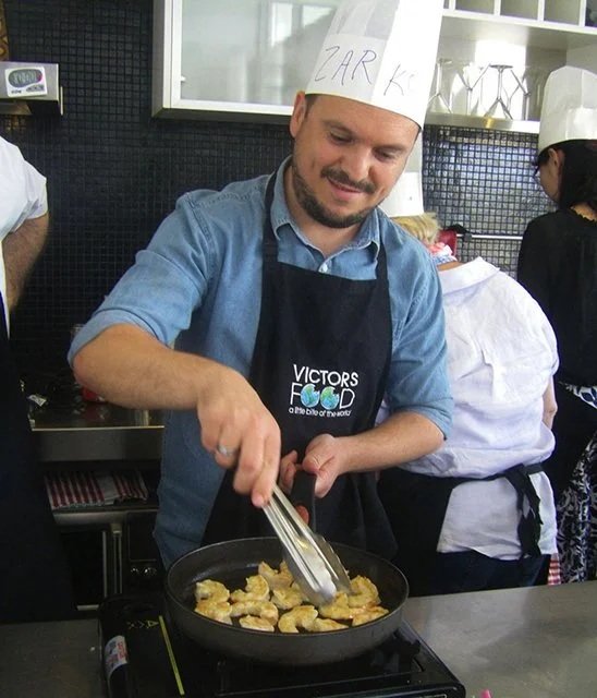 Man wearing a chef's hat with name tag 'Zark' and apron cooking food in a kitchen.