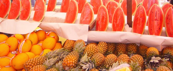 Display of sliced watermelons at a fruit stand with oranges and pineapples.