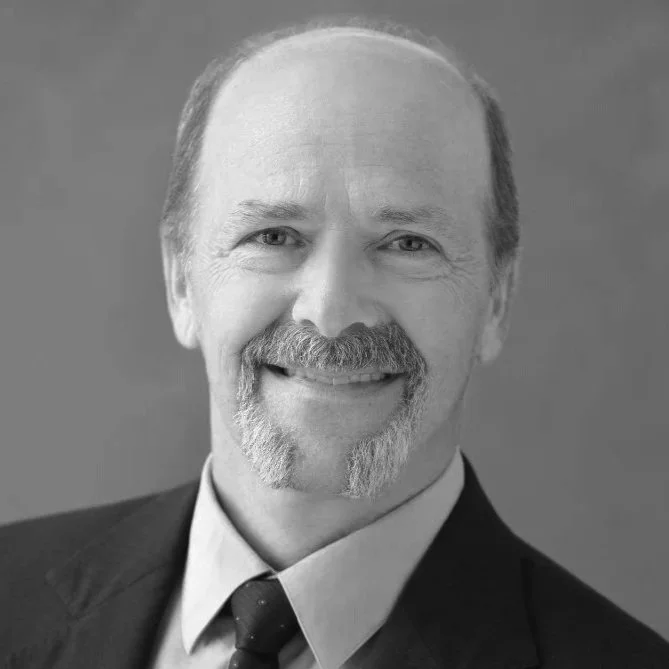 Black and white portrait of a smiling middle-aged man with a beard, mustache, and receding hairline, wearing a suit and tie.