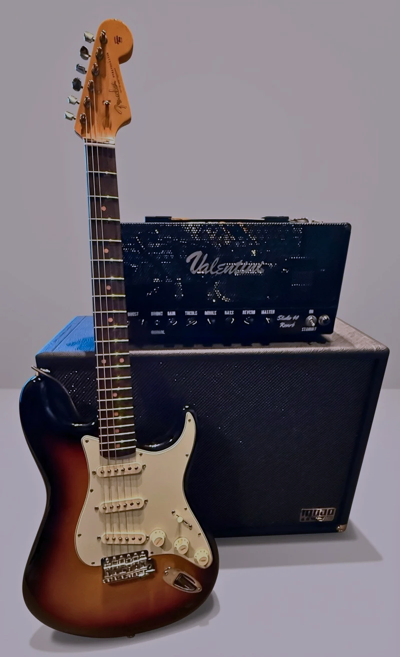 An electric guitar with a sunburst finish leaning against a black amplifier, with a smaller black amplifier on top of it, and a black speaker cabinet behind them.